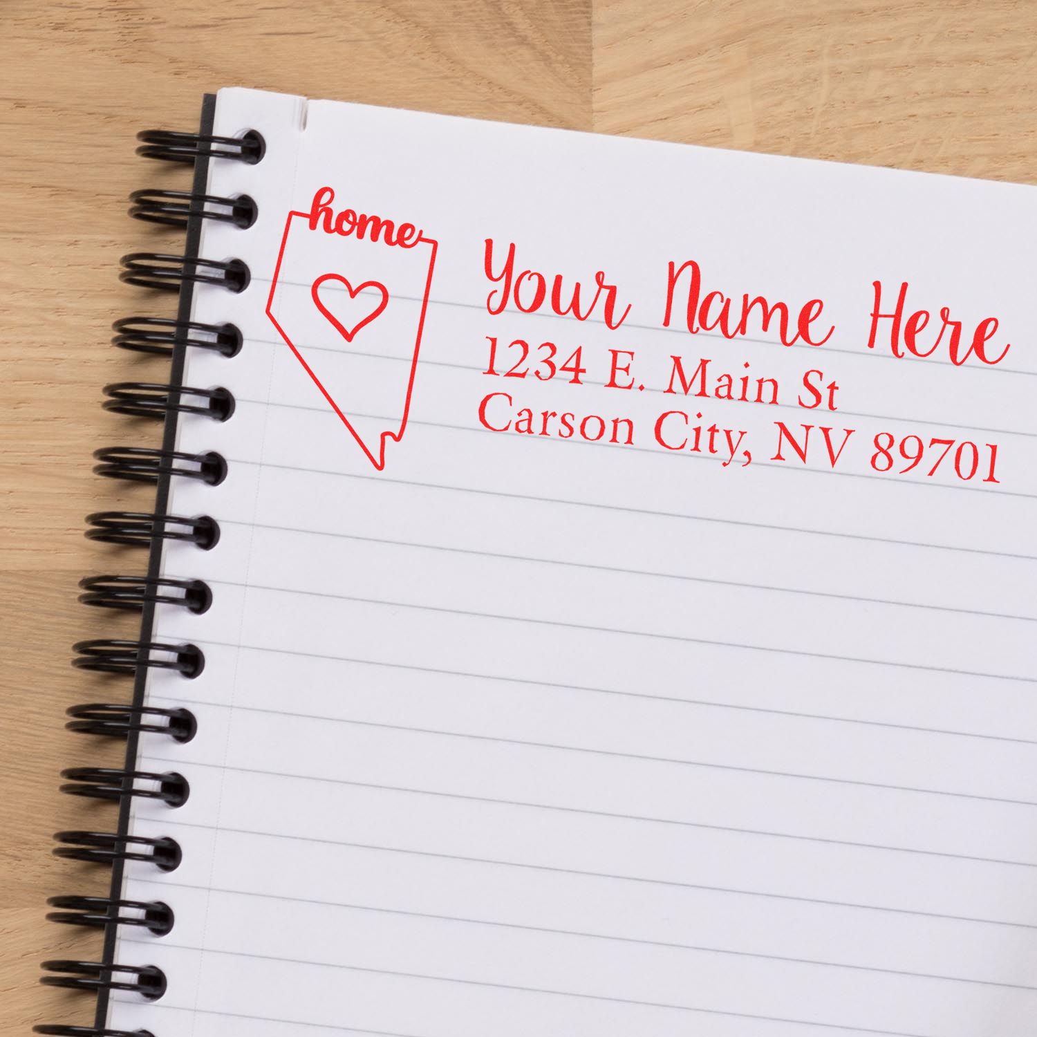 Nevada Self-Inking State Love Address Stamp on a notebook, featuring a red outline of Nevada with home text and heart, alongside customizable address fields in red ink.