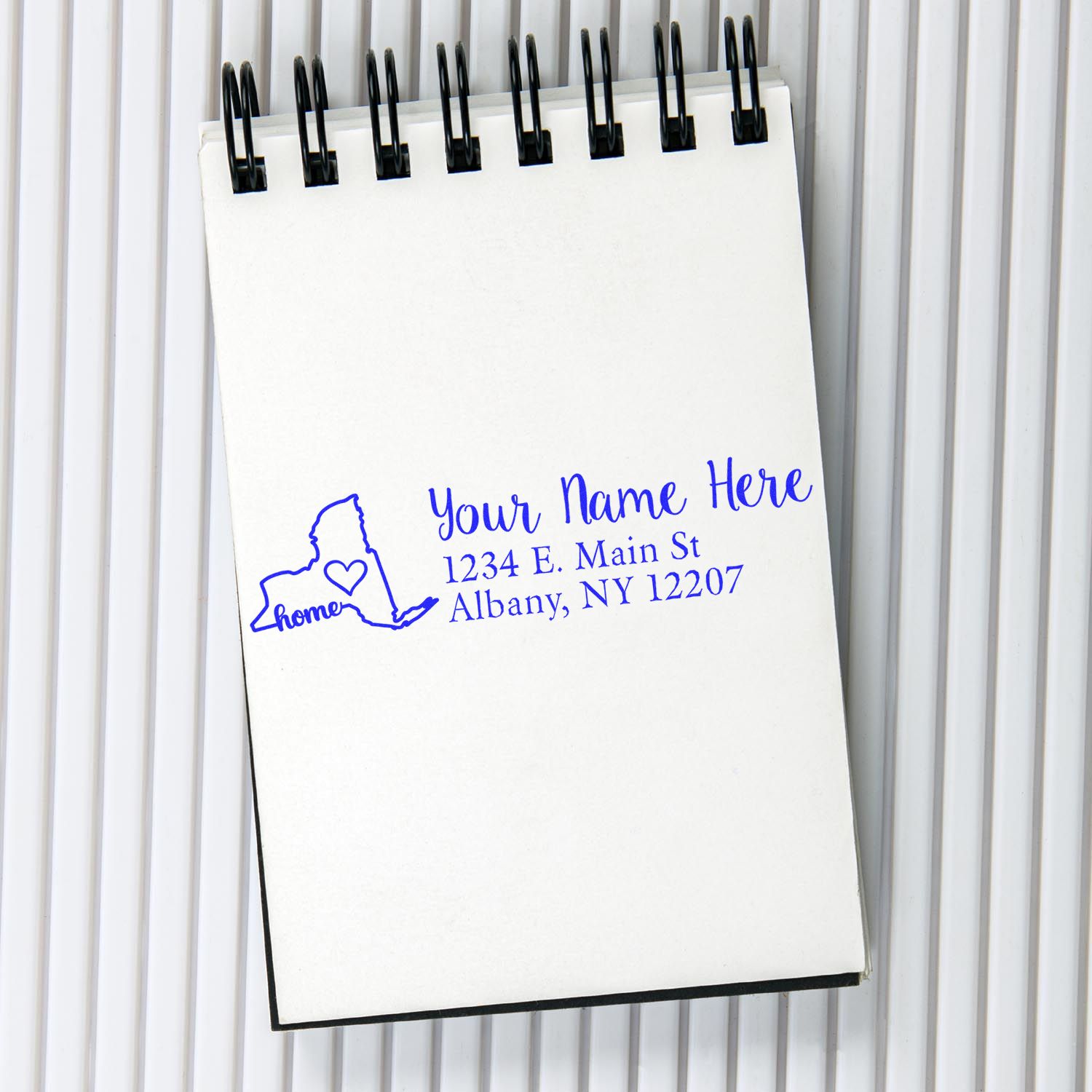 Slim Pre-Inked New York State Love Custom Address Stamp on a notepad, featuring a blue outline of New York with a heart and the word home, alongside customizable name and address fields.