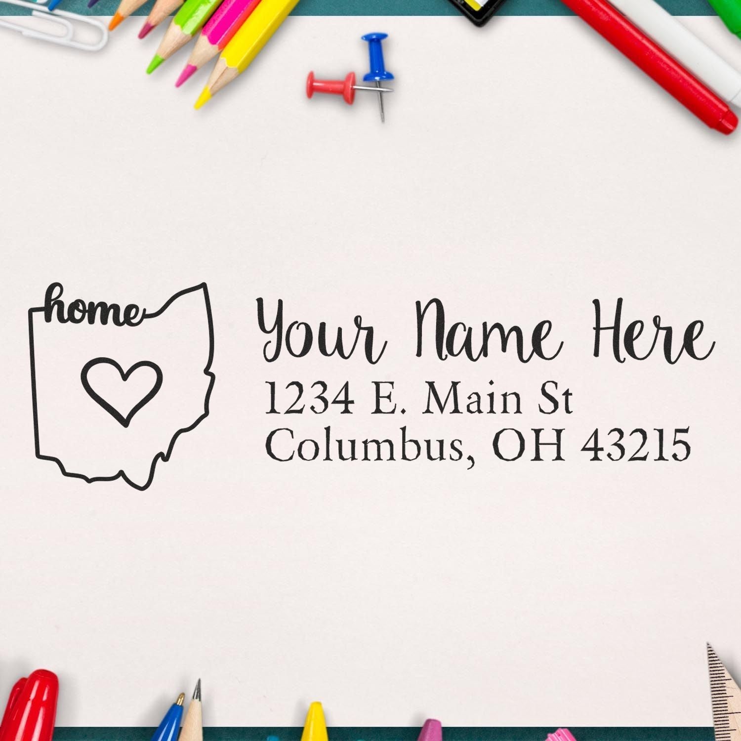 Slim Pre-Inked Ohio State Love Custom Address Stamp on paper with Your Name Here and Columbus, OH address. Surrounded by colorful pens and pins on a white background.