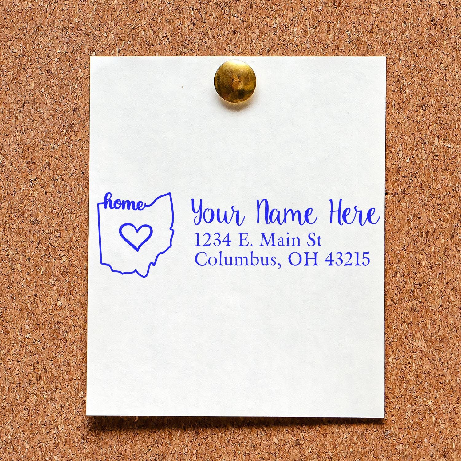 PSI Pre-Inked Personalized Ohio State Love Address Stamp on a corkboard, displaying a sample address with a heart inside the Ohio state outline, in blue ink.