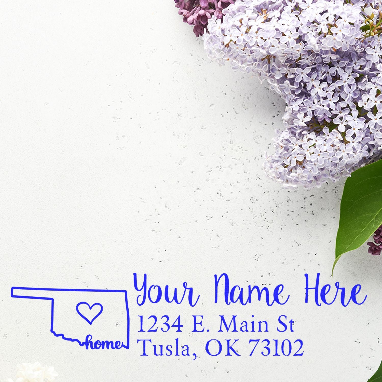 PSI Pre-Inked Personalized Oklahoma State Love Address Stamp on white paper with lilac flowers. Features a heart design within the state outline, customizable with name and address in blue ink.