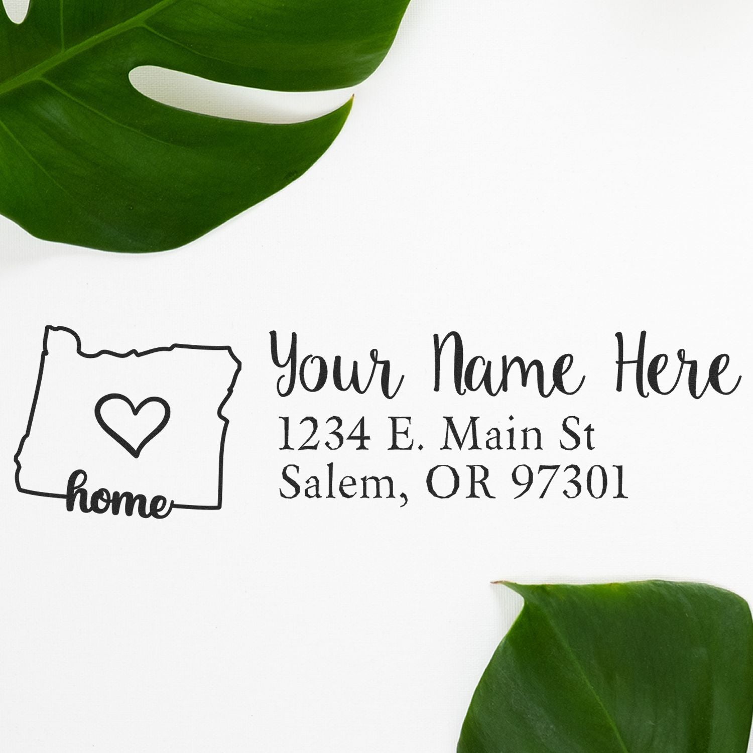 Wood Handle Oregon Custom Address Rubber Stamp with a heart design and home text, featuring a sample address. Surrounded by green leaves on a white background.