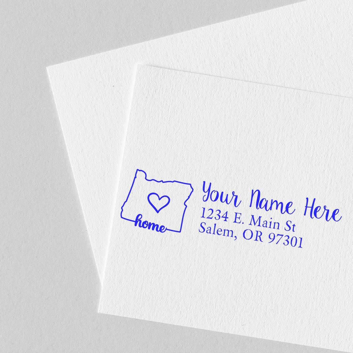 Slim Pre-Inked Oregon State Love Custom Address Stamp on white paper, featuring a blue outline of Oregon with a heart and the text Your Name Here, 1234 E. Main St, Salem, OR 97301.