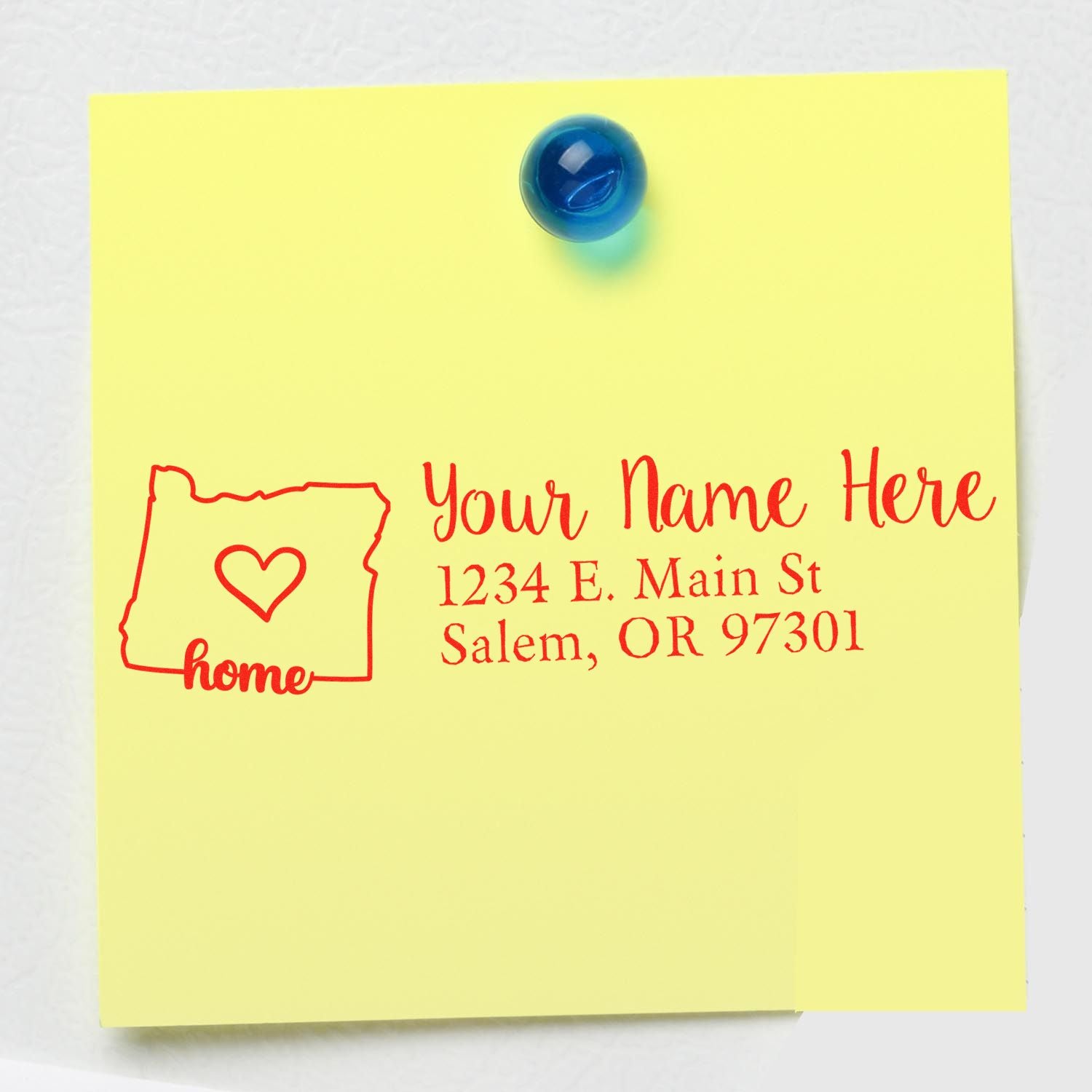 Yellow sticky note on a fridge with the Oregon Self-Inking State Love Address Stamp design, featuring a heart inside the state outline and customizable address text in red.