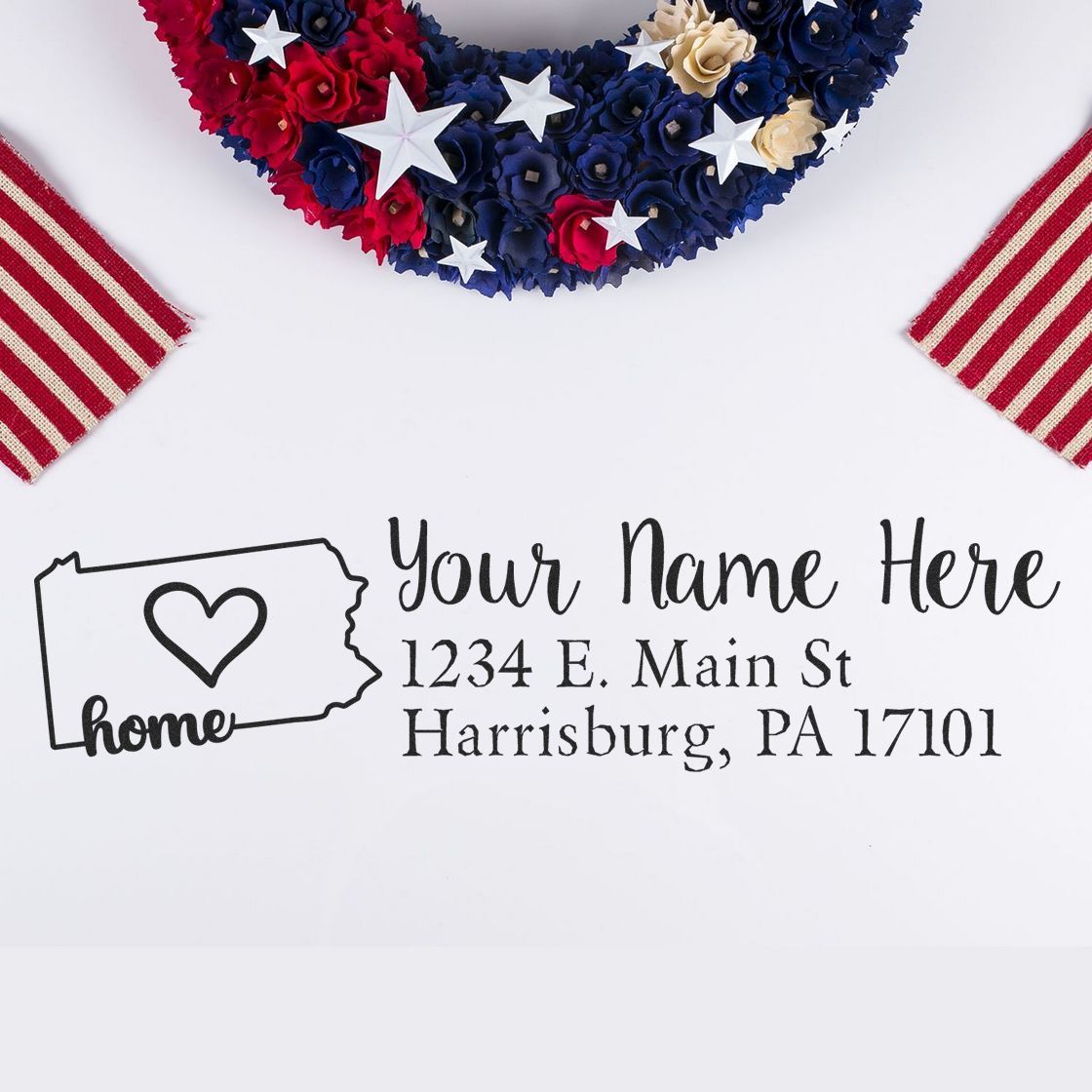 Wood Handle Pennsylvania Custom Address Rubber Stamp on a white surface, featuring a heart design within the state outline, with a patriotic wreath and striped fabric in the background.