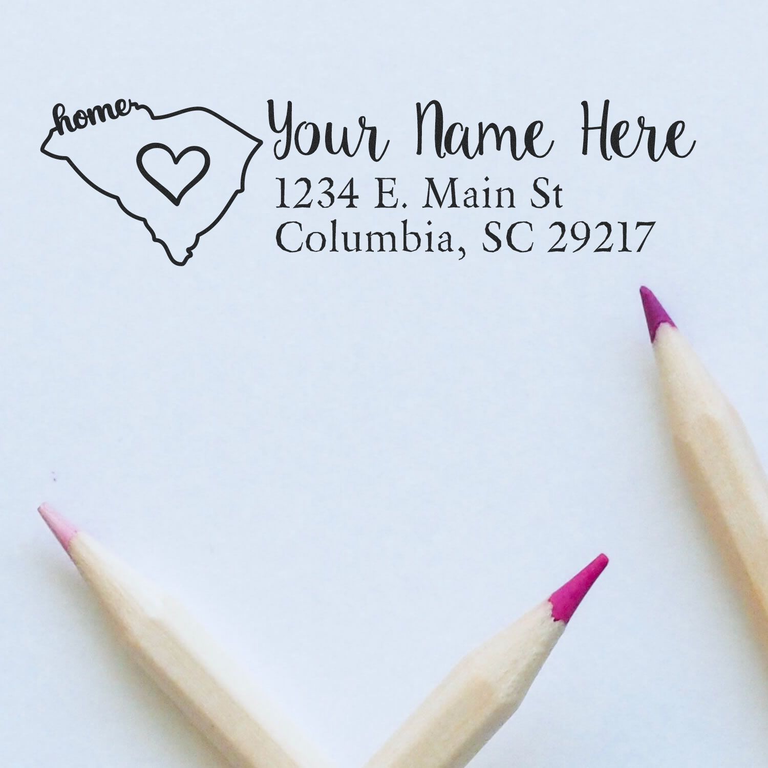 Wood Handle South Carolina Custom Address Rubber Stamp on white paper, featuring a heart within the state outline and sample address. Two pink-tipped pencils are placed below the stamped design.