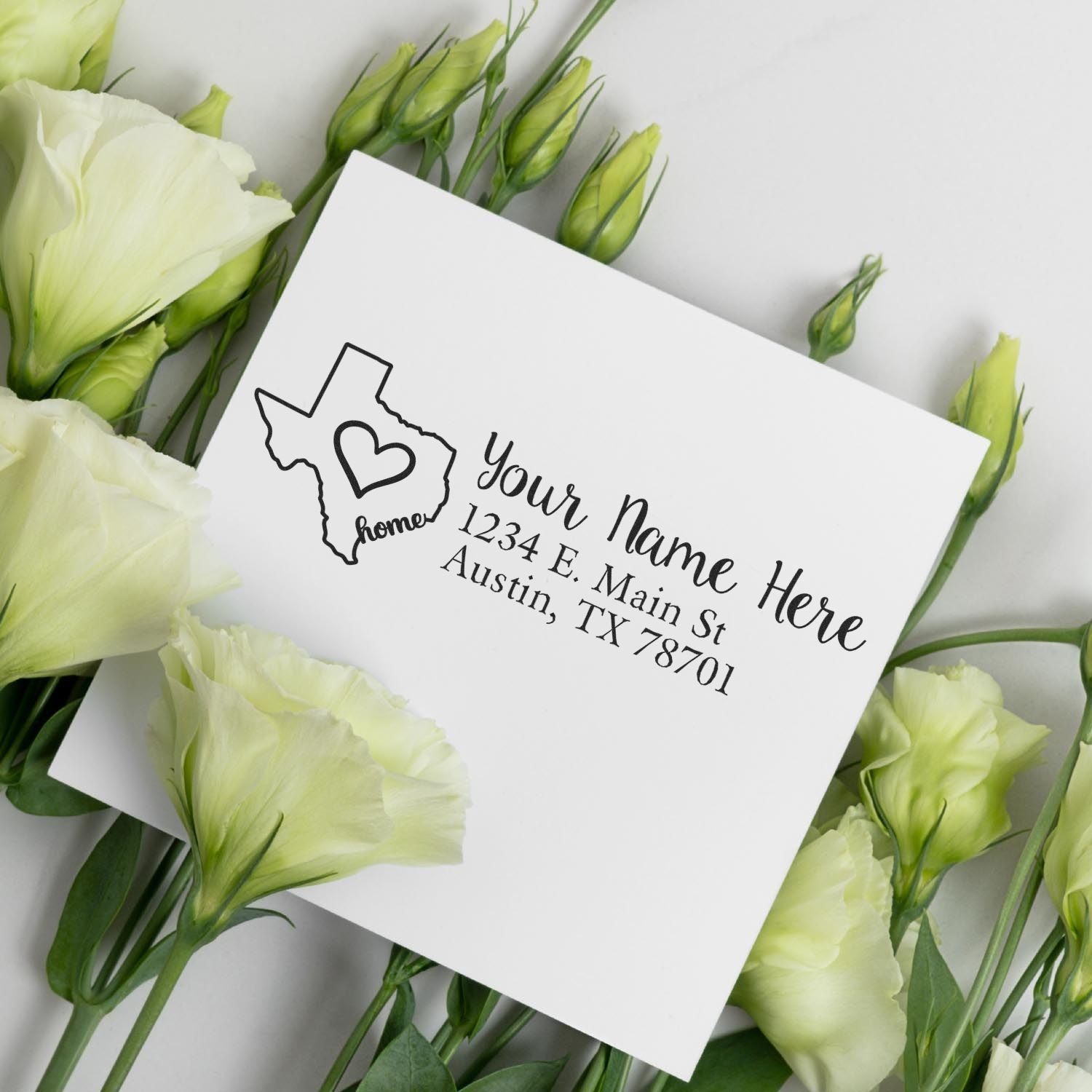 Texas Self-Inking State Love Address Stamp on a white envelope surrounded by white flowers, featuring a Texas outline with a heart and customizable address text.