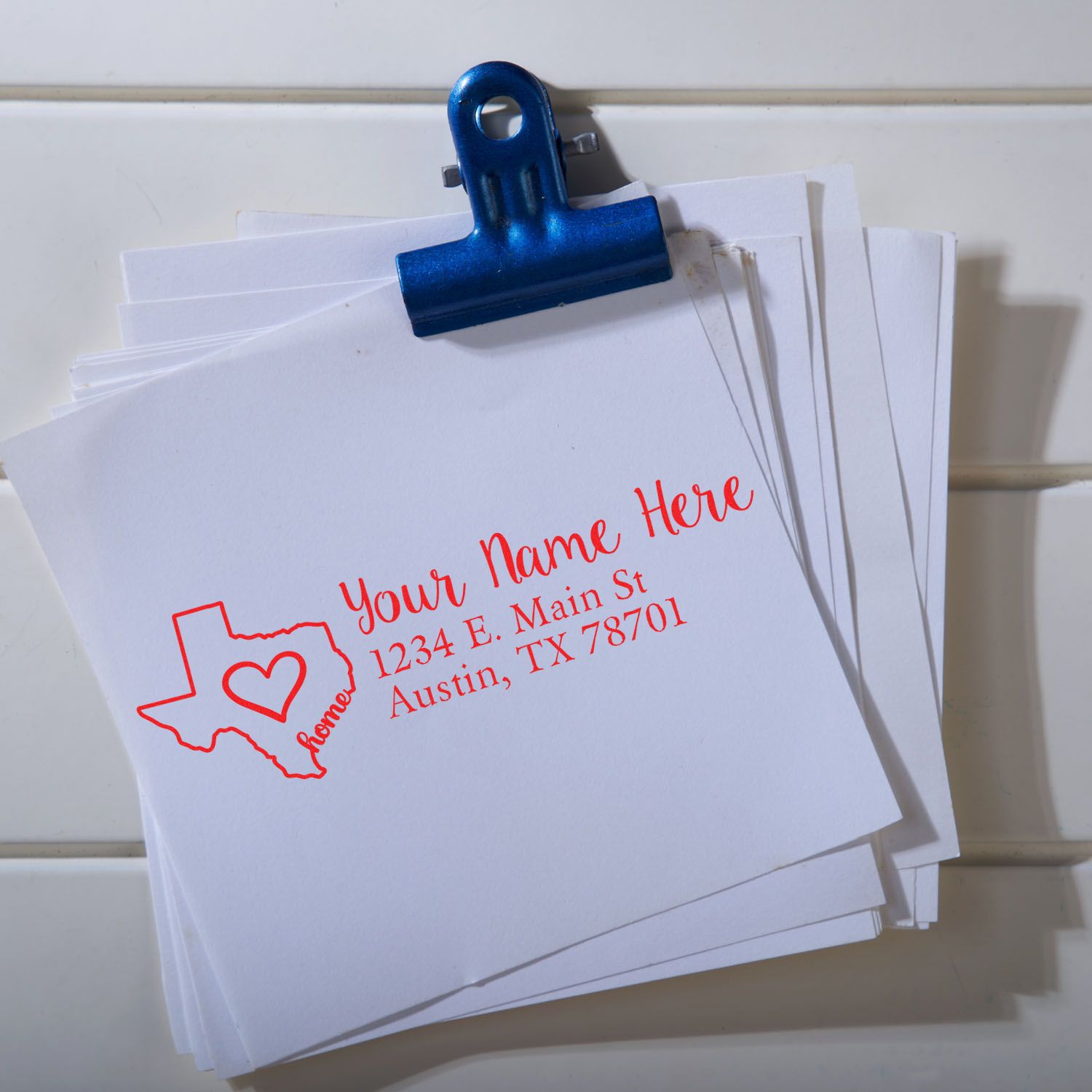 Wood Handle Texas Custom Address Rubber Stamp on white paper, featuring a red Texas outline with a heart and personalized address in red text, clipped together with a blue clip.