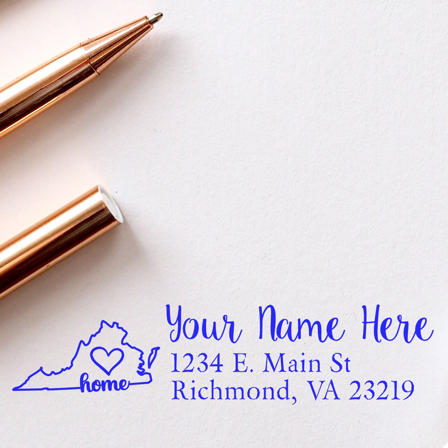 Wood Handle Virginia Custom Address Rubber Stamp on white paper, featuring a blue design with a heart in Virginia's outline, next to a rose gold pen.