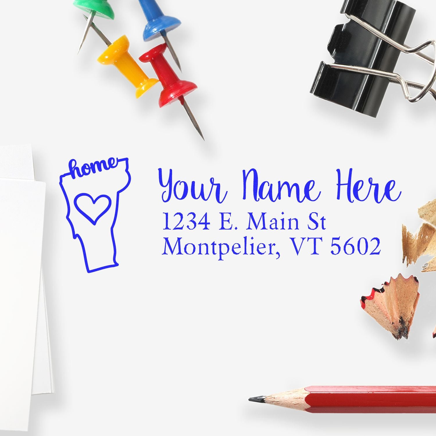 Vermont Self-Inking State Love Address Stamp on white paper, surrounded by colorful push pins, a binder clip, pencil shavings, and a red pencil.