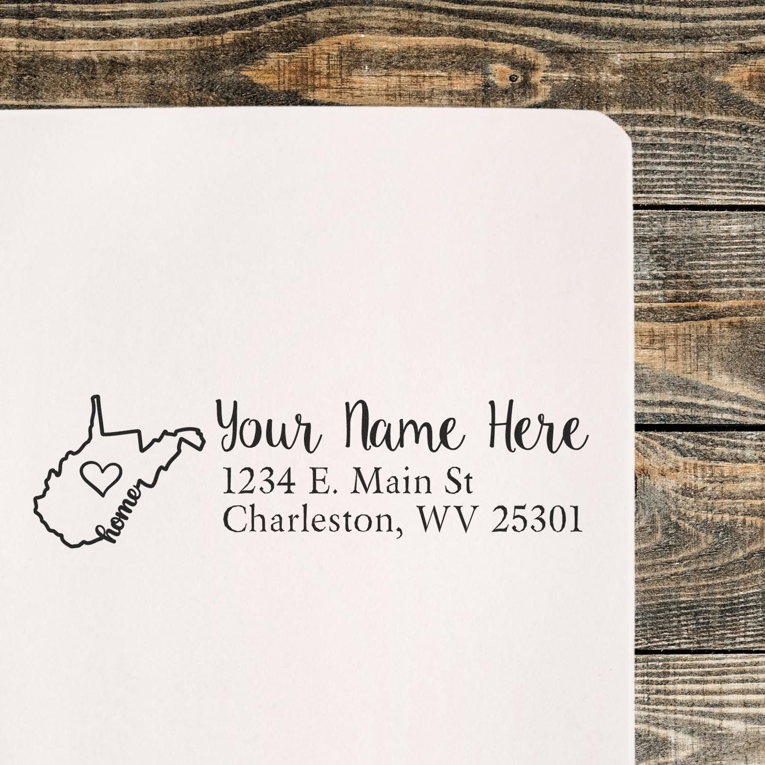 Wood Handle West Virginia Custom Address Rubber Stamp on paper, featuring a heart design within the state outline and personalized address text. Placed on a rustic wooden surface.