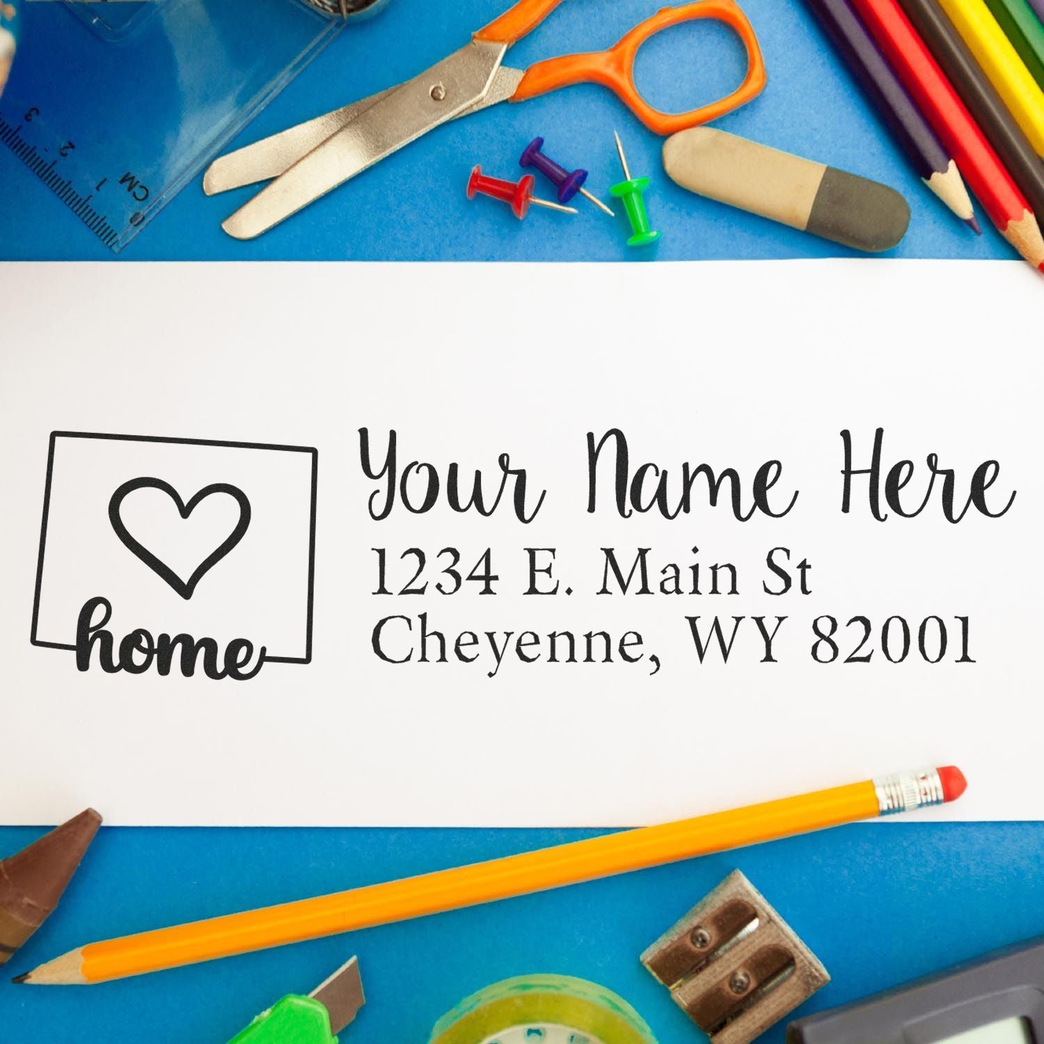 Wyoming Self-Inking State Love Address Stamp on a white envelope surrounded by colorful office supplies, including scissors, pencils, and push pins, showcasing a heart design and address text.