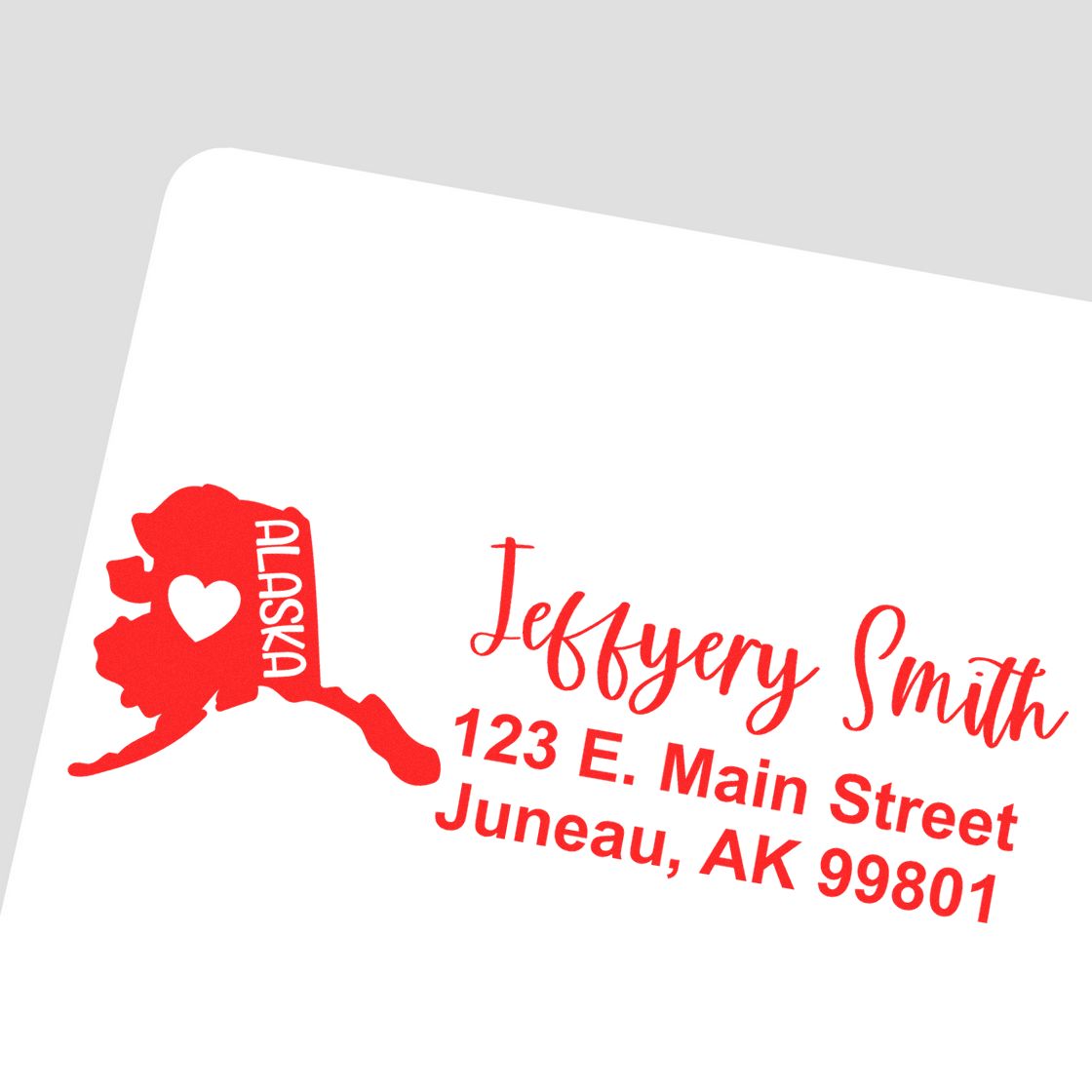 Alaska State Love Personalized Address Stamp in red ink on an envelope, featuring a heart within the Alaska state outline and custom address text for Jeffery Smith, 123 E. Main Street, Juneau, AK 99801.