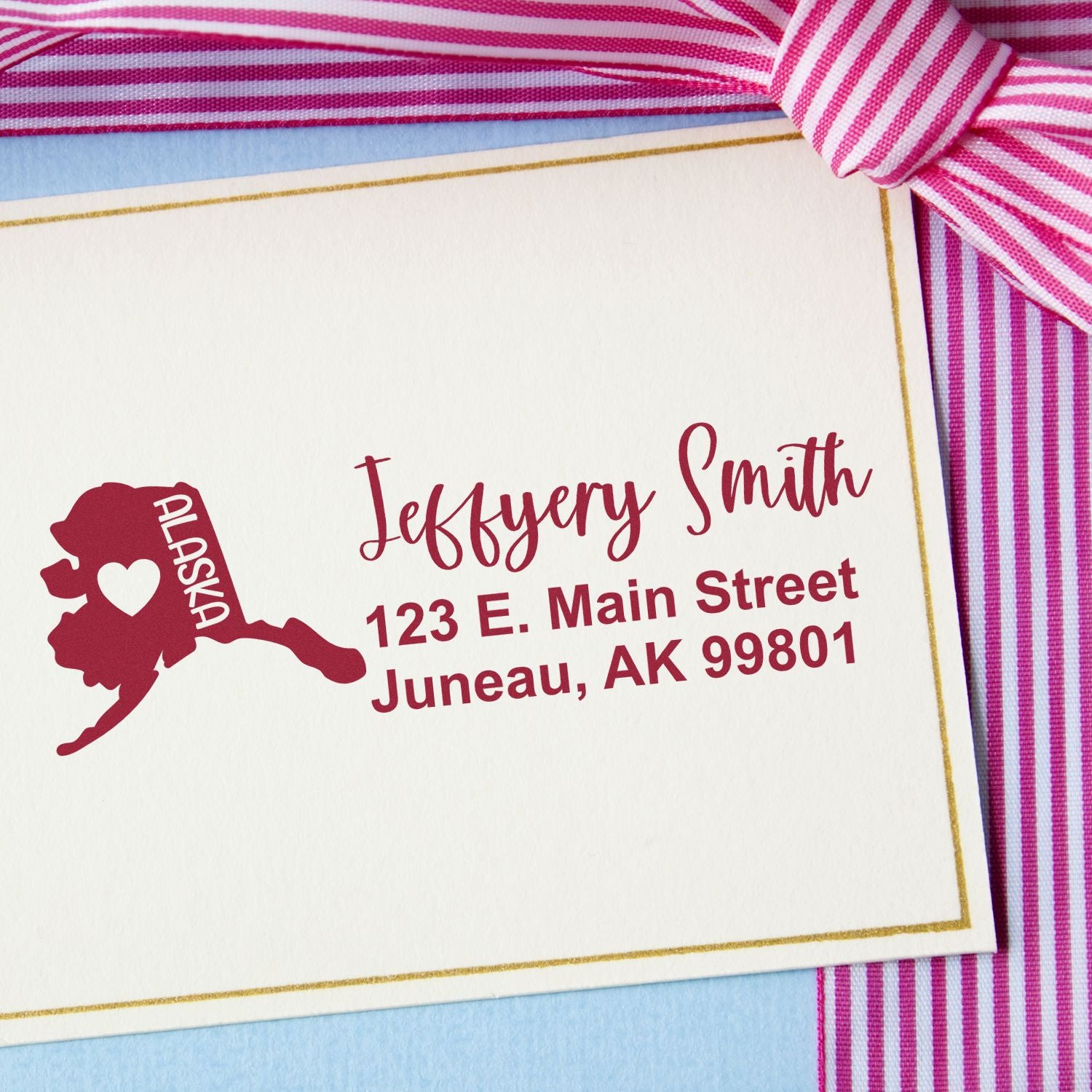 Slim Alaska Custom Address Stamp for Envelopes on a card with a pink striped ribbon, featuring a red Alaska state outline and personalized address in elegant script.