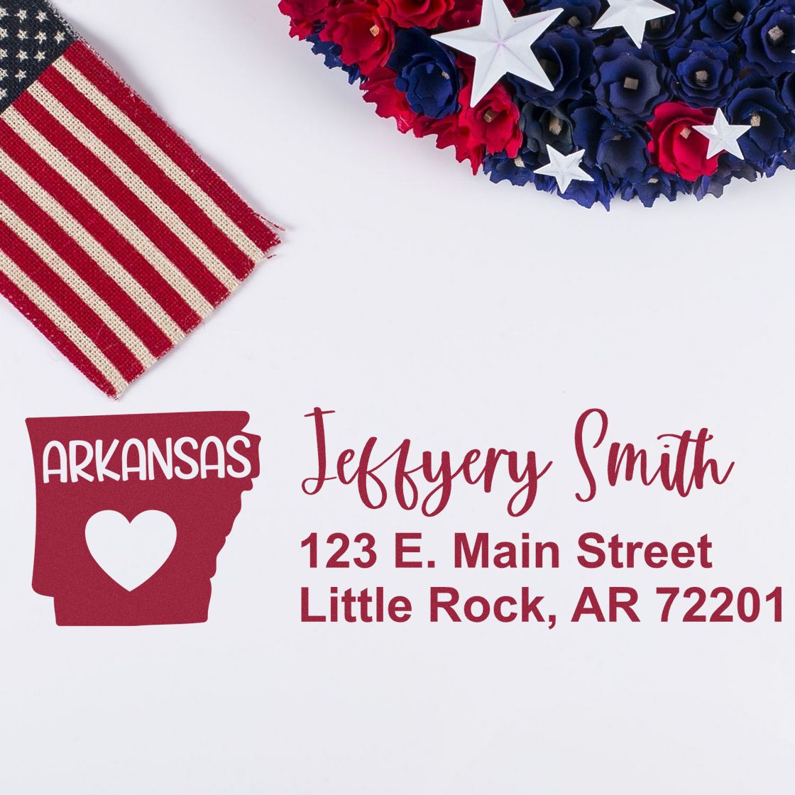 State Love of Arkansas Custom Address Stamp Self-Inking displayed with a patriotic theme, featuring an Arkansas silhouette with a heart, next to an American flag and red, white, and blue flowers.