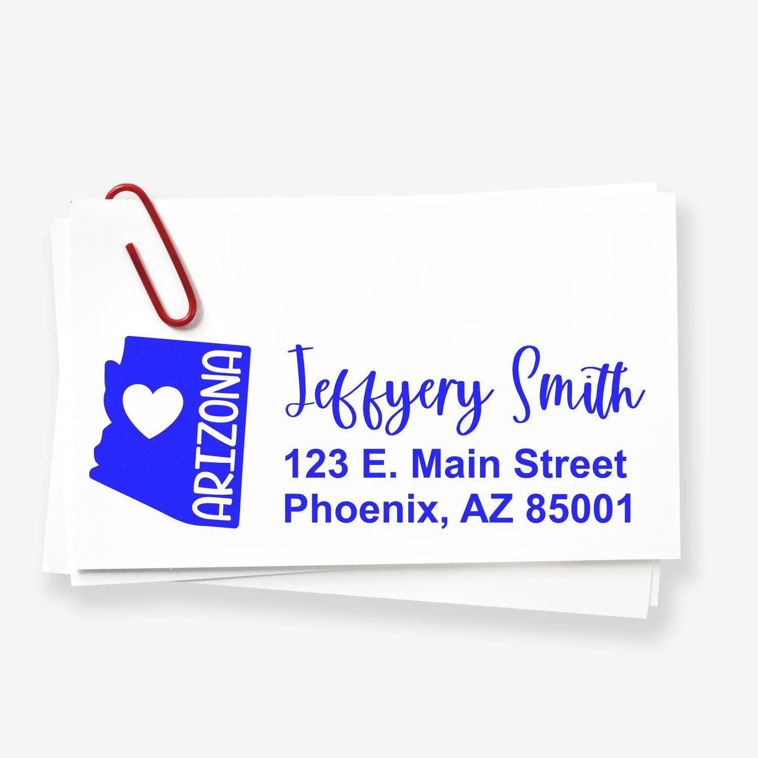 Slim Arizona Custom Address Stamp for Envelopes displayed on white paper with a red paperclip. Features a blue Arizona state outline with a heart and personalized address in bold, stylish font.