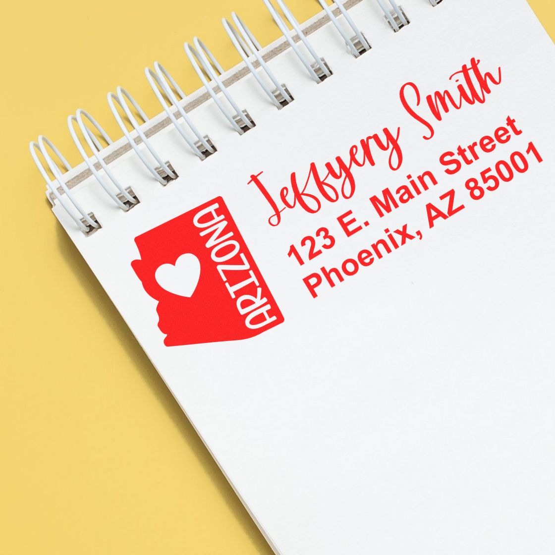 Slim Arizona Custom Address Stamp for Envelopes displayed on a notepad, featuring a red Arizona state outline with a heart, personalized with name and address in bold red text.