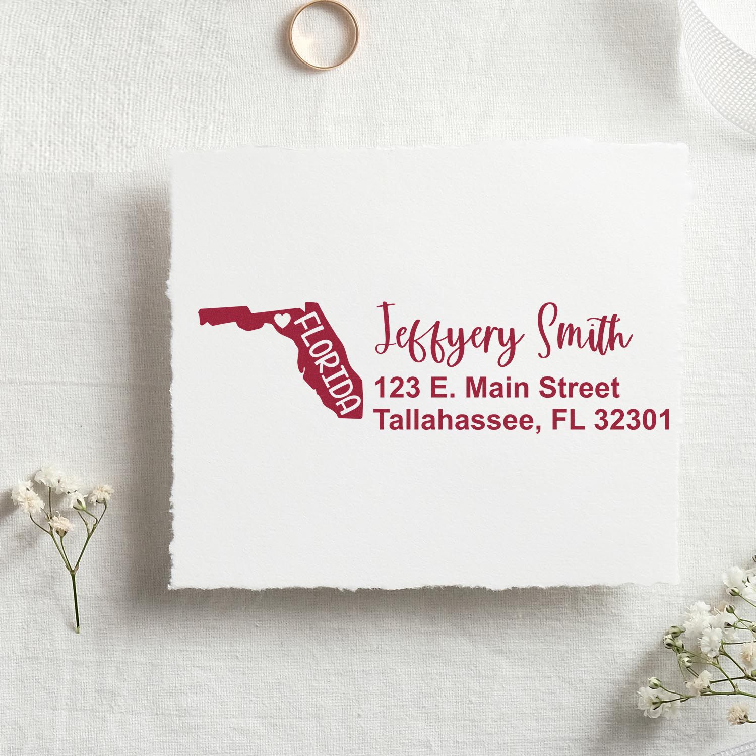 State Love of Florida Custom Address Stamp Self-Inking on white paper, featuring a red Florida map design with personalized address details. Set on a textured surface with small flowers and a ring nearby.