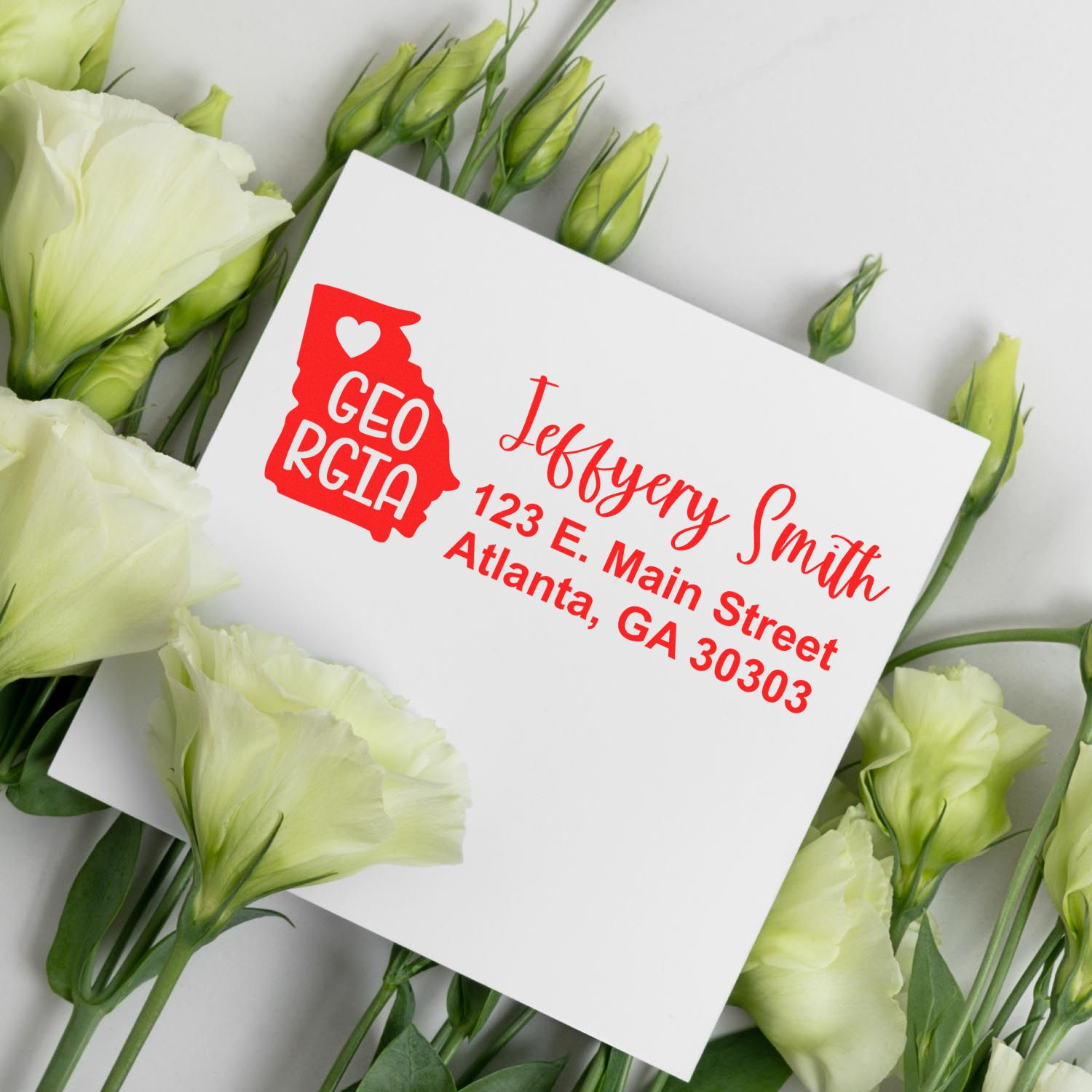 Slim Georgia Custom Address Stamp for Envelopes displayed on a white card with green and white flowers, featuring a red Georgia state outline and personalized address in elegant script.