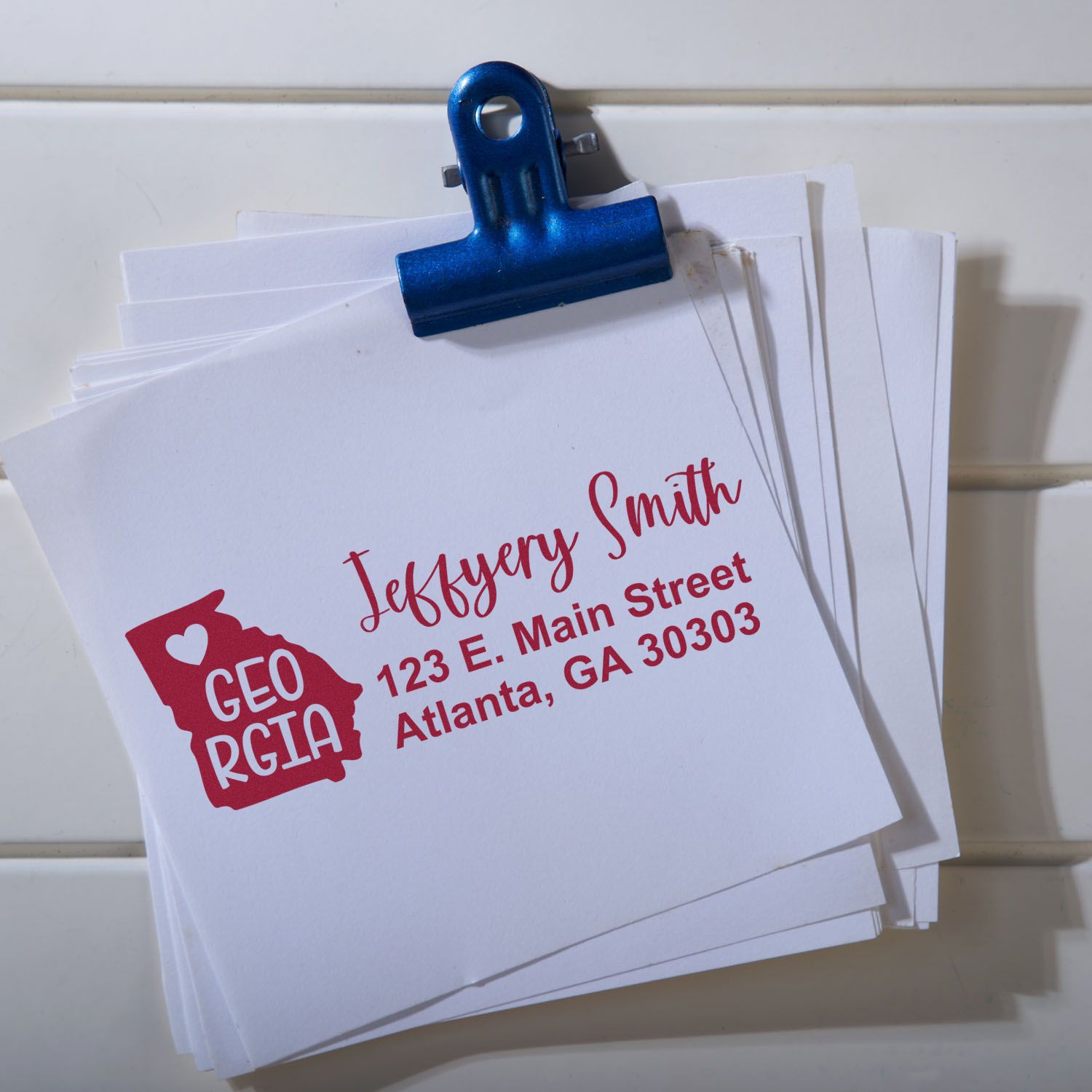 A stack of envelopes featuring the Slim Georgia Custom Address Stamp, showcasing a red design with a heart and state outline, personalized with a name and address in bold, elegant font.