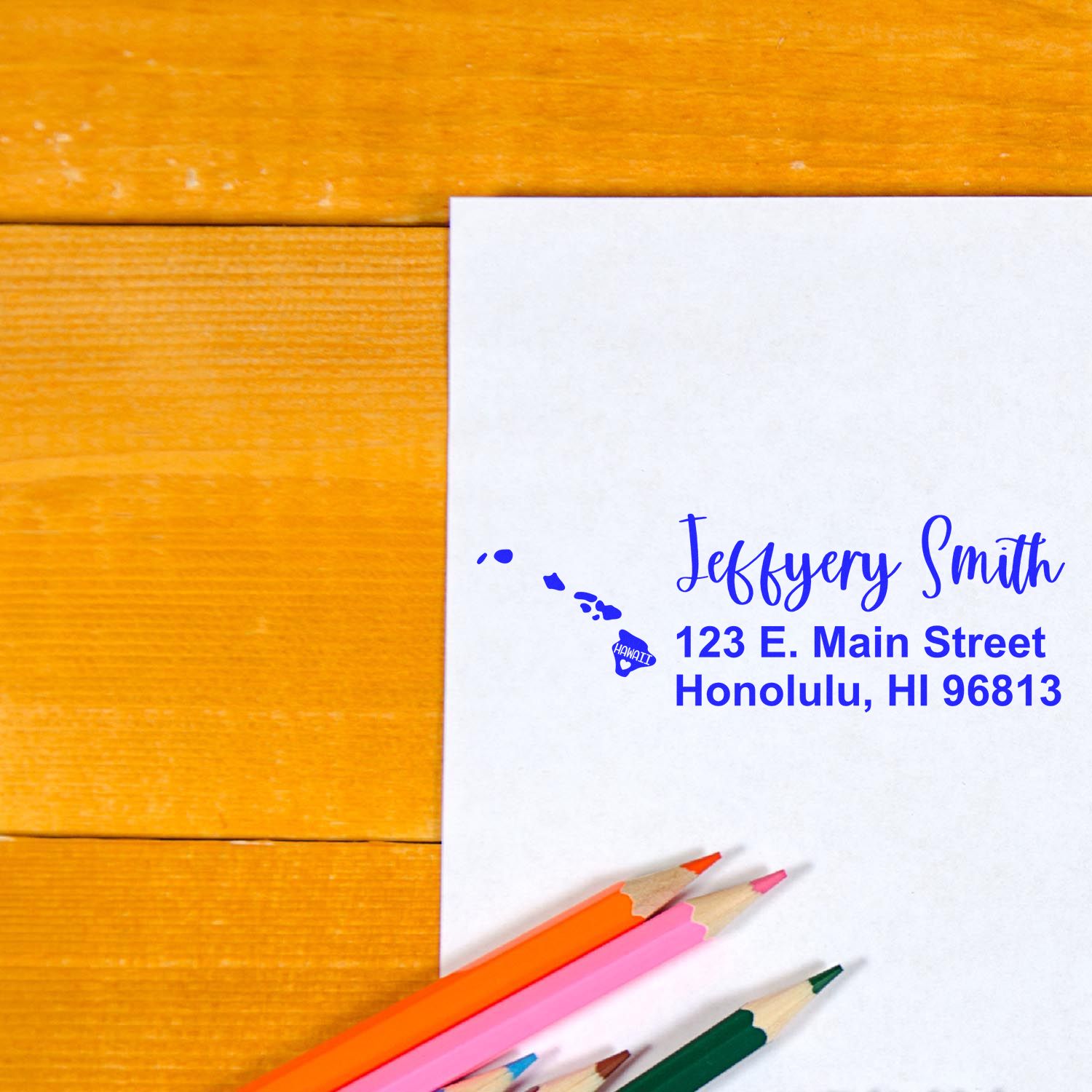 Hawaii State Love Personalized Address Stamp on white paper with blue ink, featuring a map of Hawaii and address details. Colored pencils are placed nearby on a wooden surface.