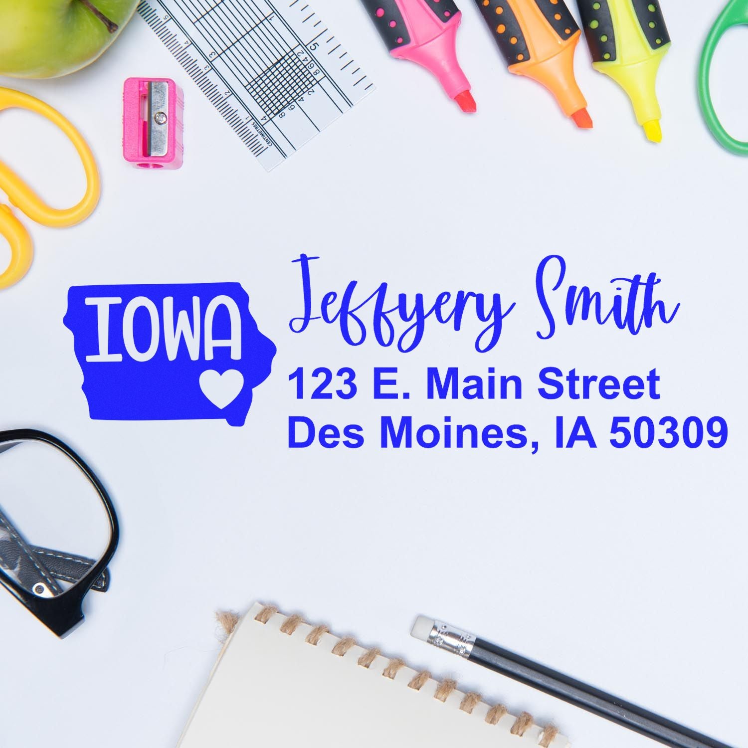 Desk with stationery items and a State Love of Iowa Custom Address Stamp Self-Inking imprint showing Jeffery Smith, 123 E. Main Street, Des Moines, IA 50309 in blue ink on white paper.