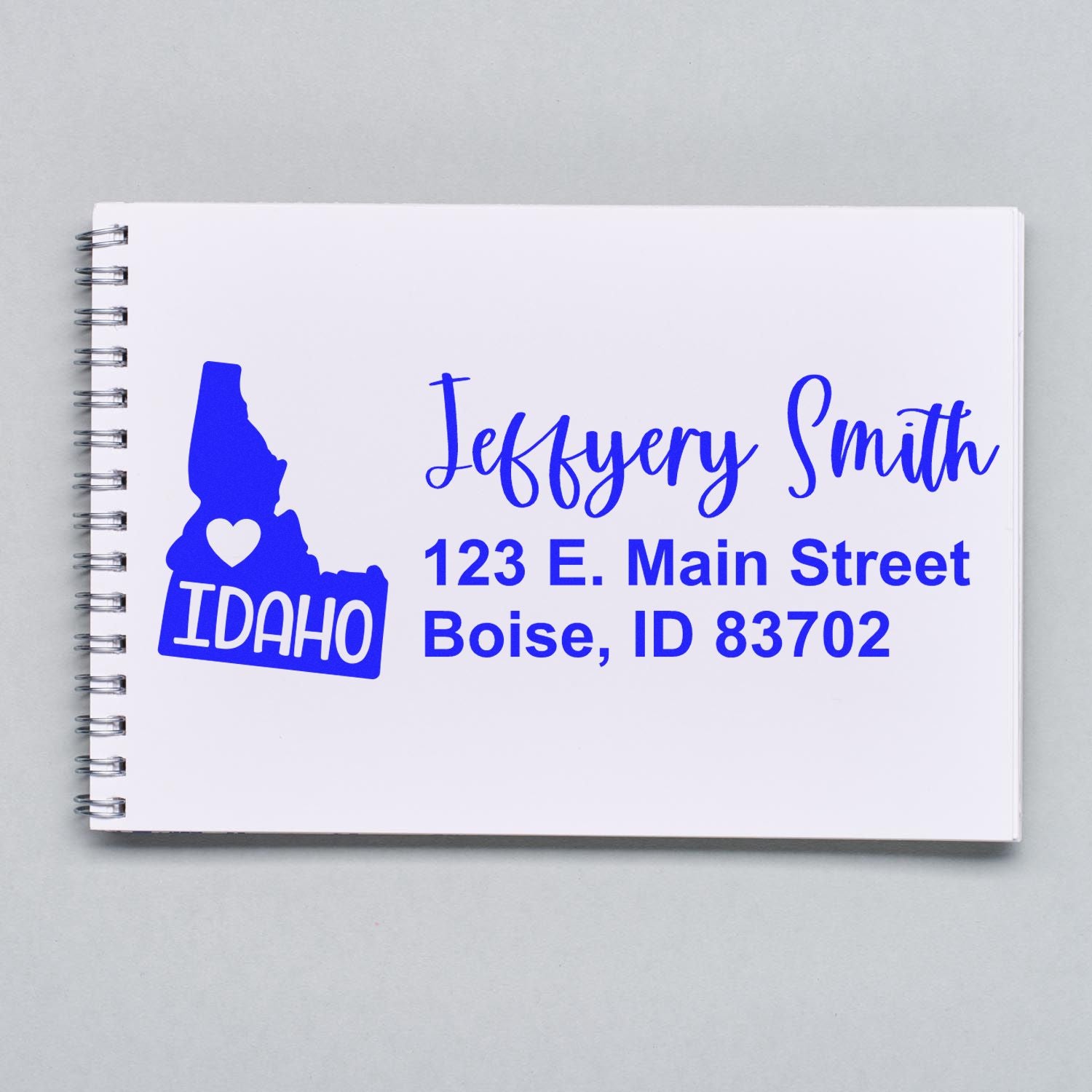 State Love of Idaho Custom Address Stamp Self-Inking displayed on a notebook, featuring a blue Idaho state outline with a heart and personalized address in bold blue text.