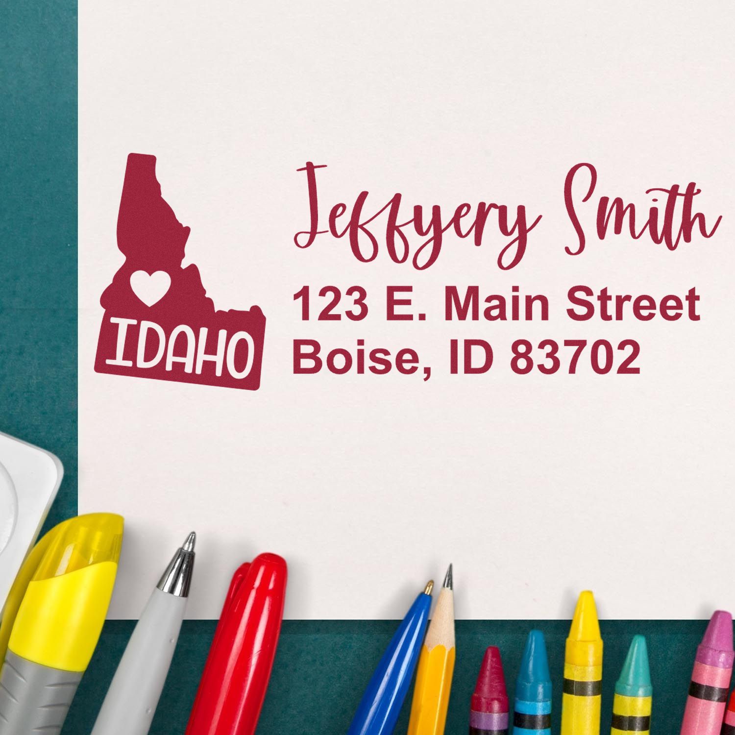 State Love of Idaho Custom Address Stamp Self-Inking displayed on paper with colorful pens, featuring a heart and Idaho state outline, personalized with name and address in red ink.