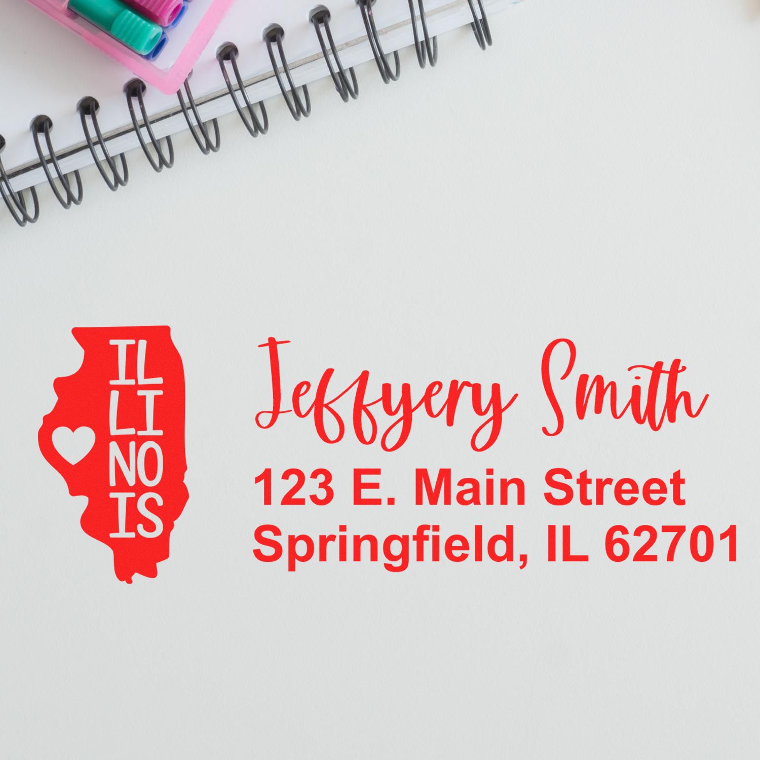 Illinois State Love Personalized Address Stamp in red ink on paper, featuring a heart design within the state outline, next to a notebook and colored pens.