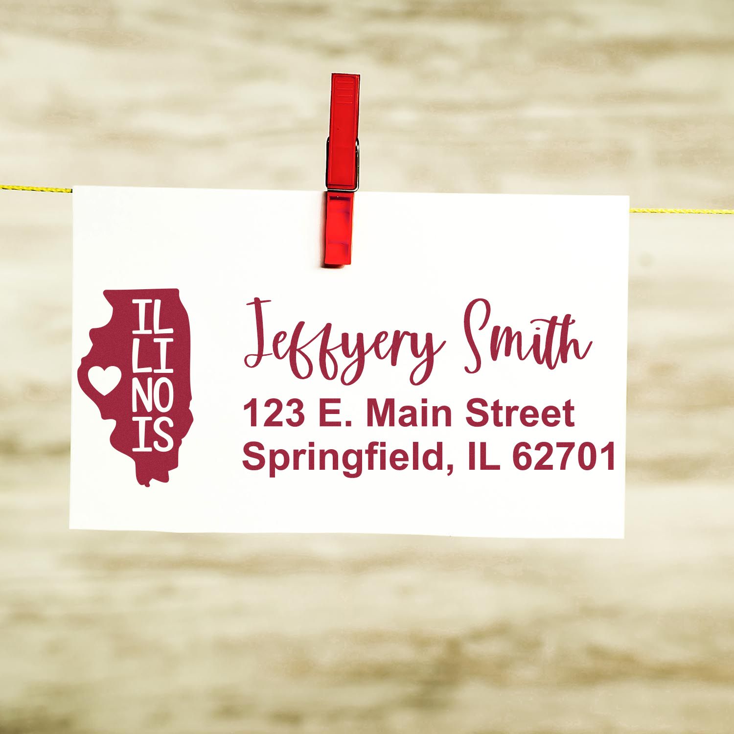 PSI Pre-Inked Illinois State Love Customized Address Stamp on a card with Jeffery Smith, 123 E. Main Street, Springfield, IL 62701 in red text, clipped to a line with a red clothespin.