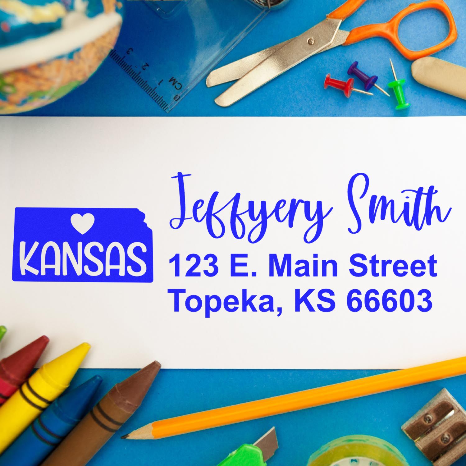 Kansas State Love Personalized Address Stamp on an envelope with colorful stationery items like scissors, pins, and crayons surrounding it. The stamp features a heart and the word KANSAS.