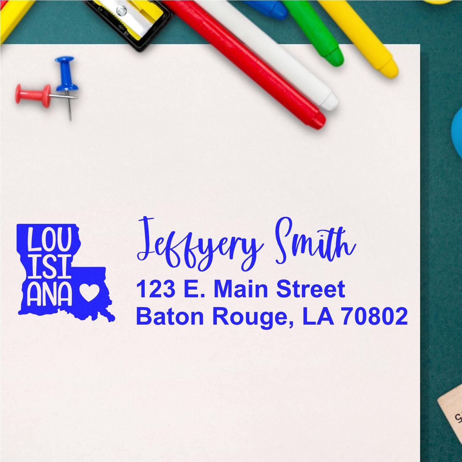 State Love of Louisiana Custom Address Stamp Self-Inking displayed on white paper with colorful pens and push pins, featuring a Louisiana state outline and personalized address in blue ink.