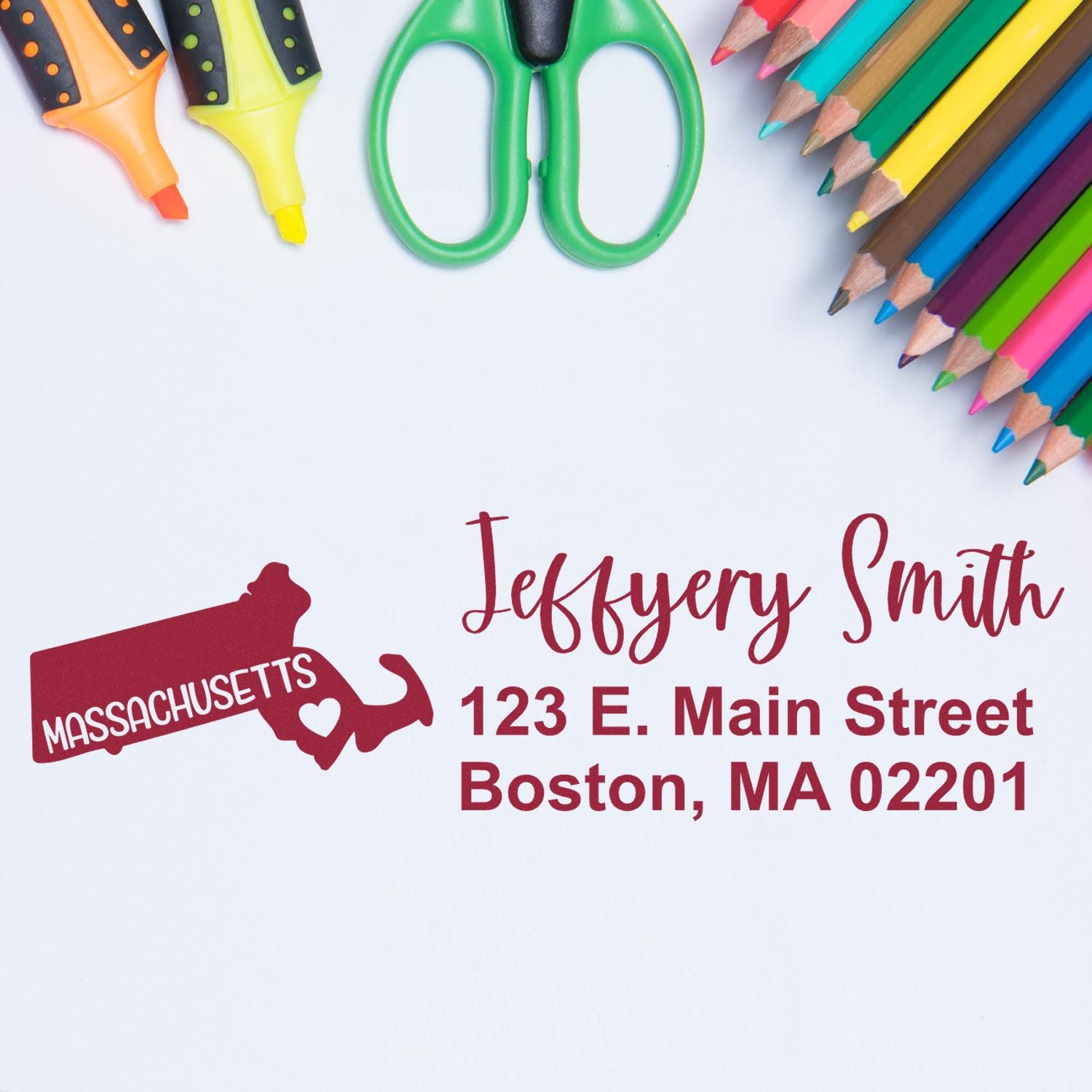 State Love of Massachusetts Custom Address Stamp Self-Inking displayed on paper with colorful pencils and scissors, featuring a Massachusetts state outline and personalized address in red.