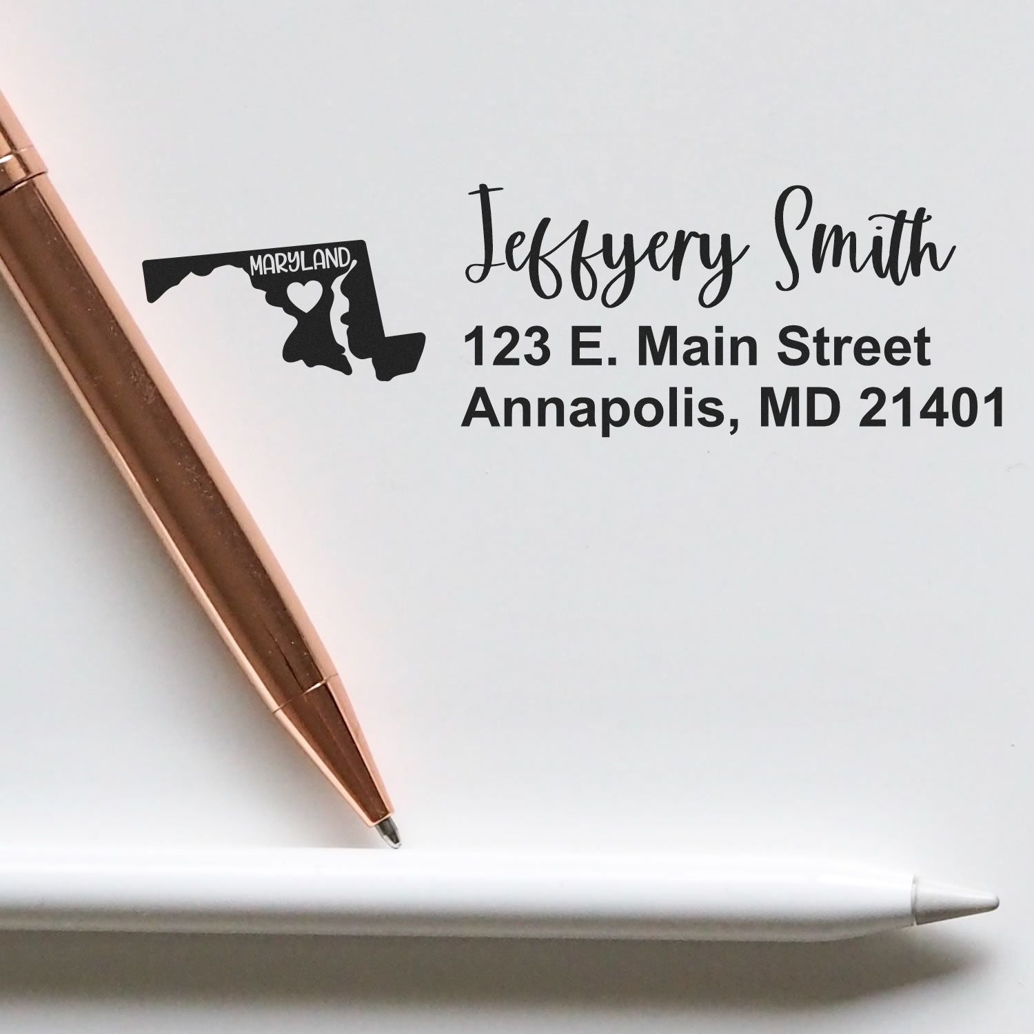 PSI Pre-Inked Maryland State Love Customized Address Stamp on paper with a rose gold pen and white pencil, featuring a Maryland map design and personalized address for Jeffery Smith in Annapolis, MD.