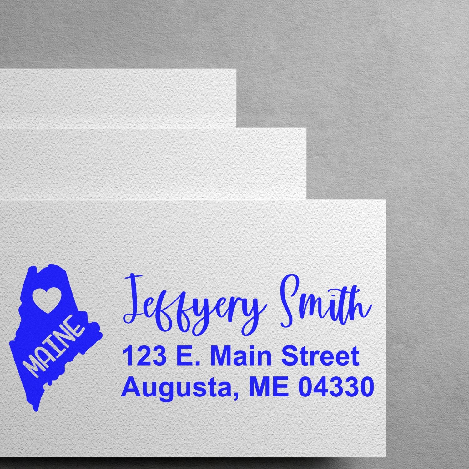 PSI Pre-Inked Maine State Love Customized Address Stamp on white envelopes, featuring a blue Maine state outline with a heart and personalized address in blue script font.