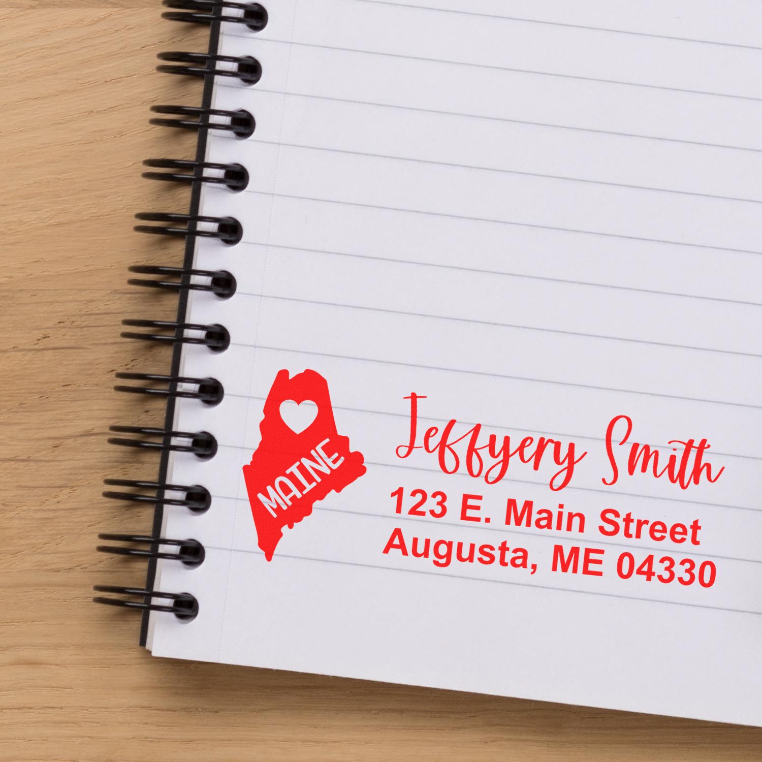 State Love of Maine Custom Address Stamp Self-Inking on a notebook page, featuring a red Maine outline with a heart and personalized address: Jeffery Smith, 123 E. Main Street, Augusta, ME 04330.