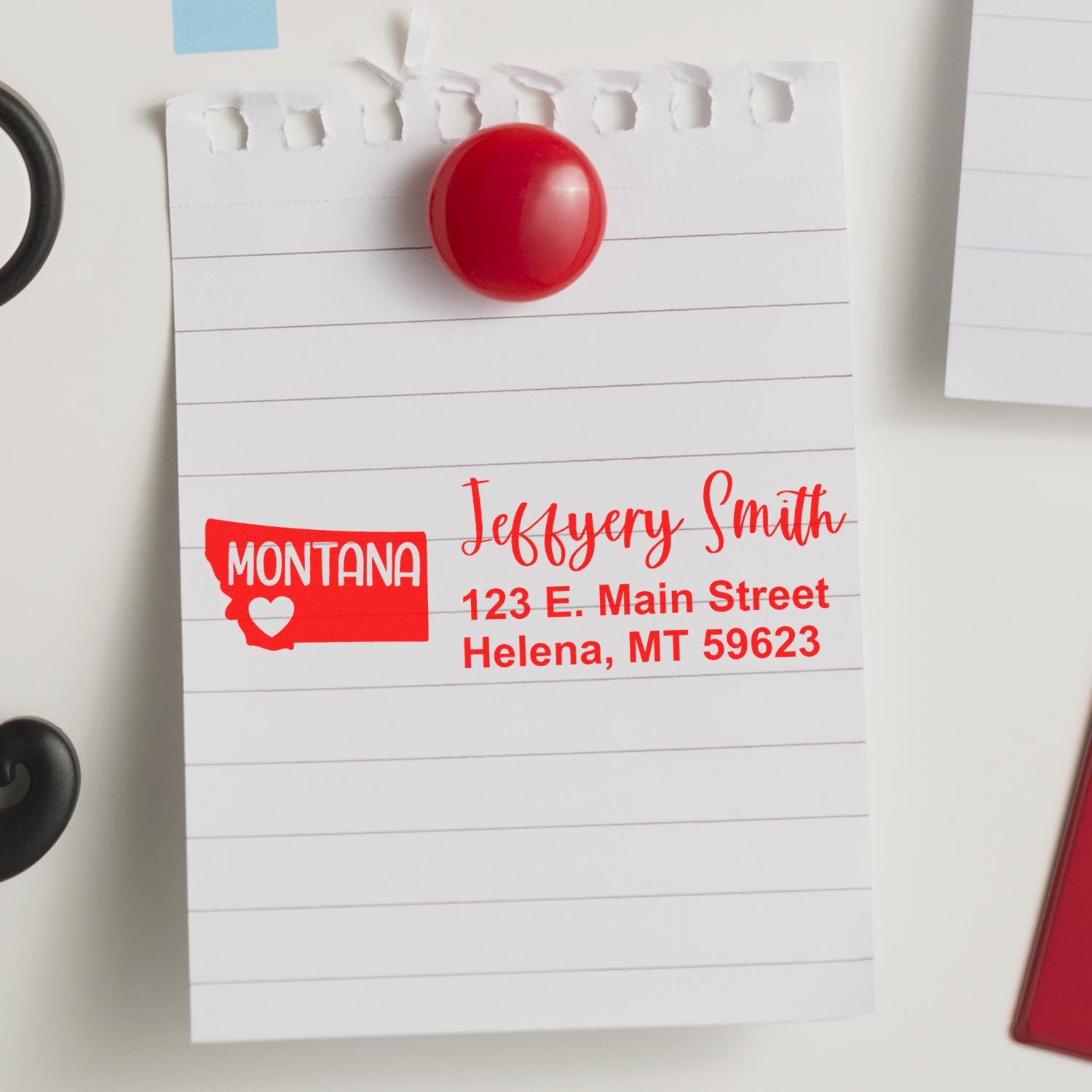 Slim Montana Custom Address Stamp for Envelopes displayed on a lined notepad, featuring a red Montana state outline and personalized address in bold red text.