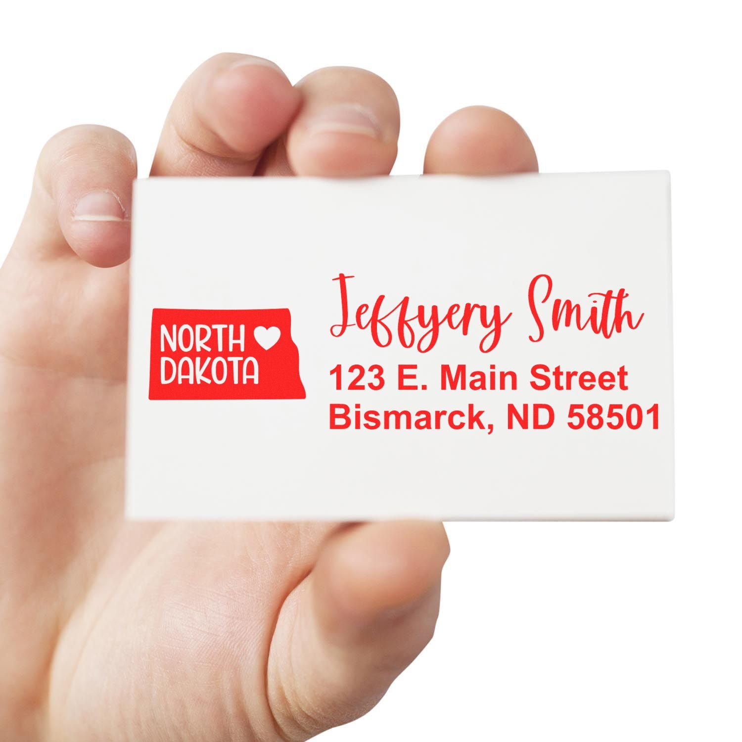 Hand holding a North Dakota State Love Personalized Address Stamp with red text: Jeffery Smith, 123 E. Main Street, Bismarck, ND 58501 and a North Dakota state outline with a heart.