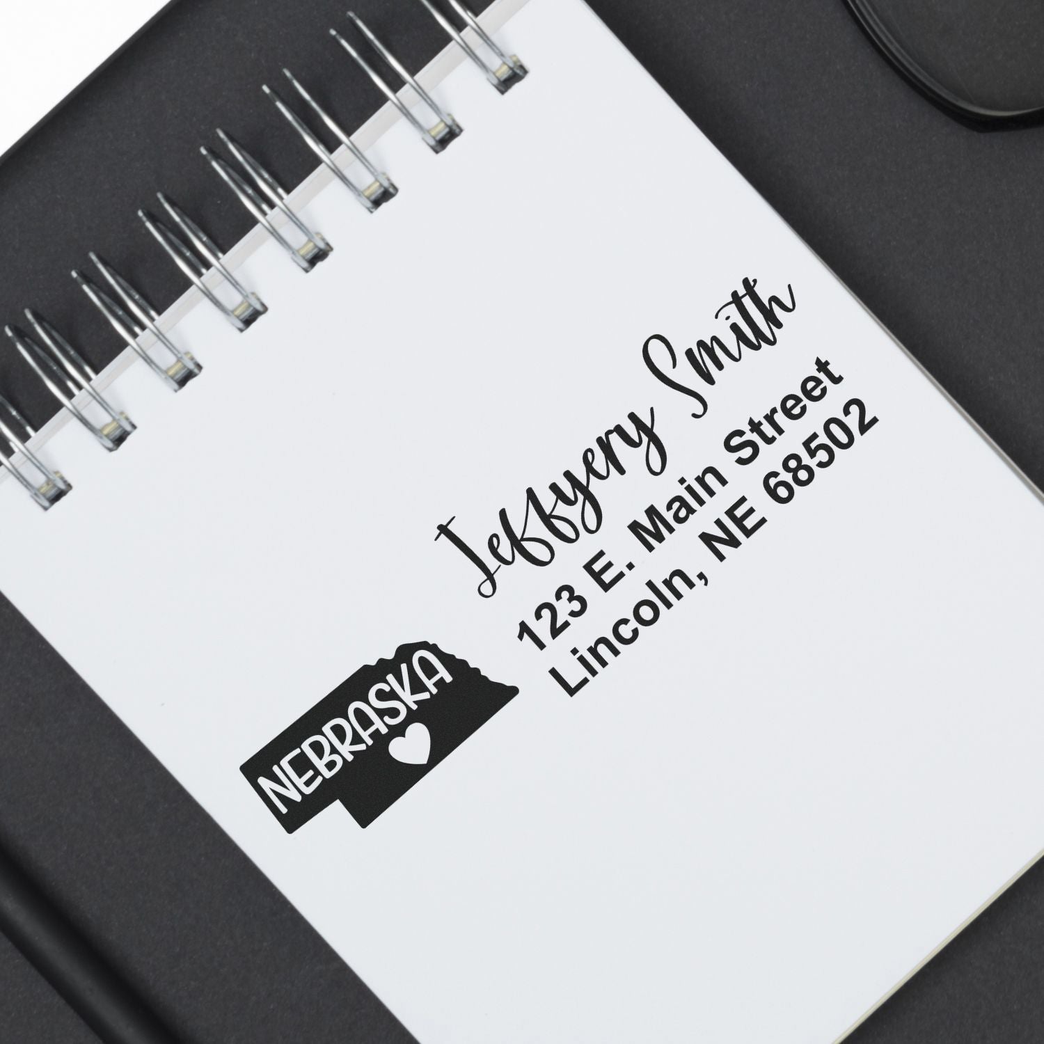 Close-up of a notebook page stamped with the Nebraska State Love Personalized Address Stamp, featuring a Nebraska outline, heart, and sample address in elegant black font.