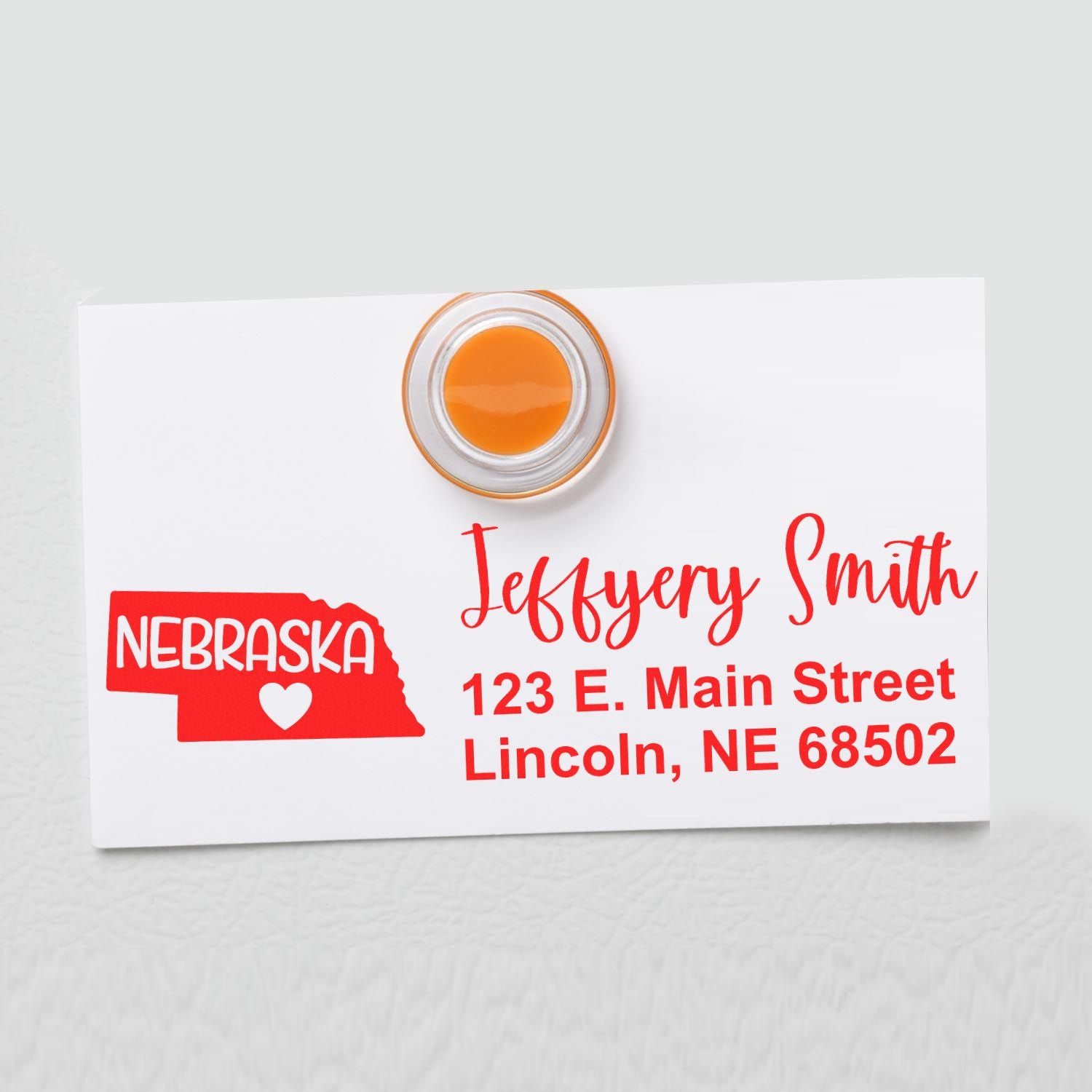 Nebraska State Love Personalized Address Stamp on a white card with red text, featuring a Nebraska state outline and heart. Address: 123 E. Main Street, Lincoln, NE 68502. Orange magnet on top.