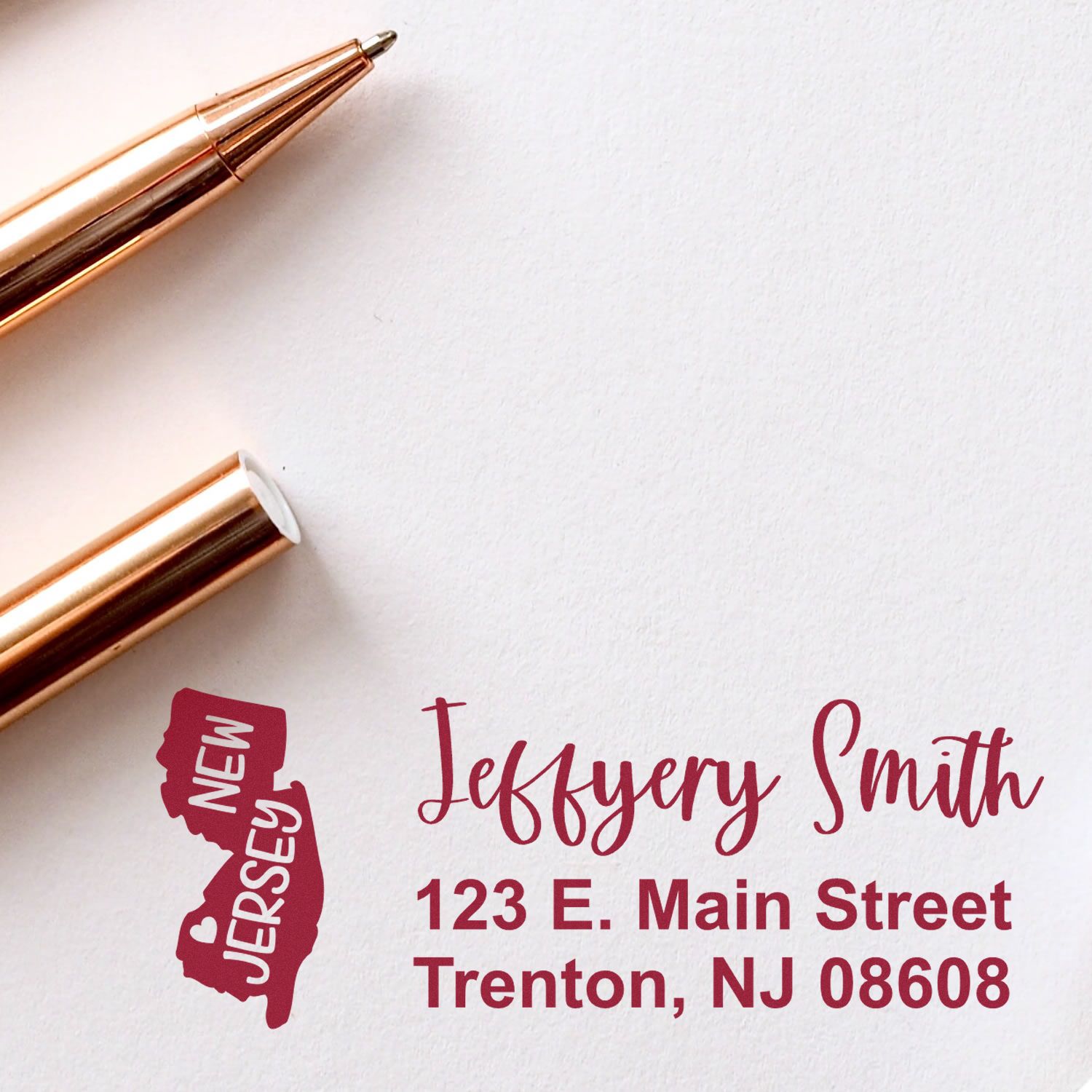 Image of a PSI Pre-Inked New Jersey State Love Customized Address Stamp on an envelope, featuring a New Jersey state outline and personalized address in red ink, next to a gold pen.