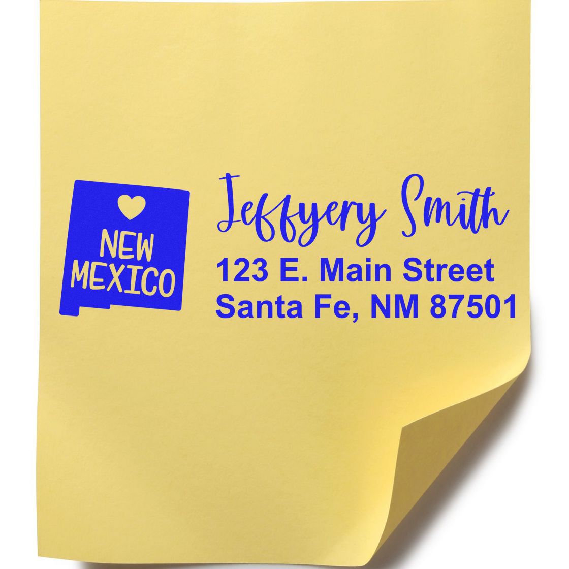 Yellow paper with blue ink showing the State Love of New Mexico Custom Address Stamp Self-Inking design, featuring a heart and state outline, personalized with a name and Santa Fe address.