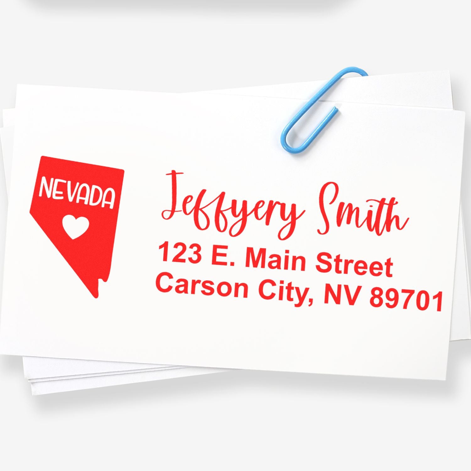 Nevada State Love Personalized Address Stamp on white paper, featuring a red Nevada map with a heart, and red text for name and address. A blue paperclip holds the stack together.