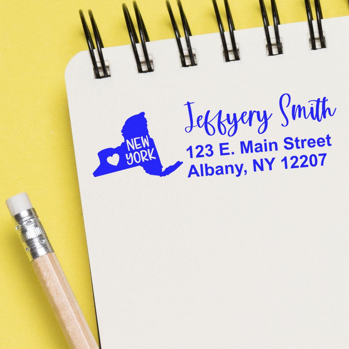 State Love of New York Custom Address Stamp Self-Inking displayed on a notepad with a pencil. The stamp shows a blue New York state outline with a heart and address details.