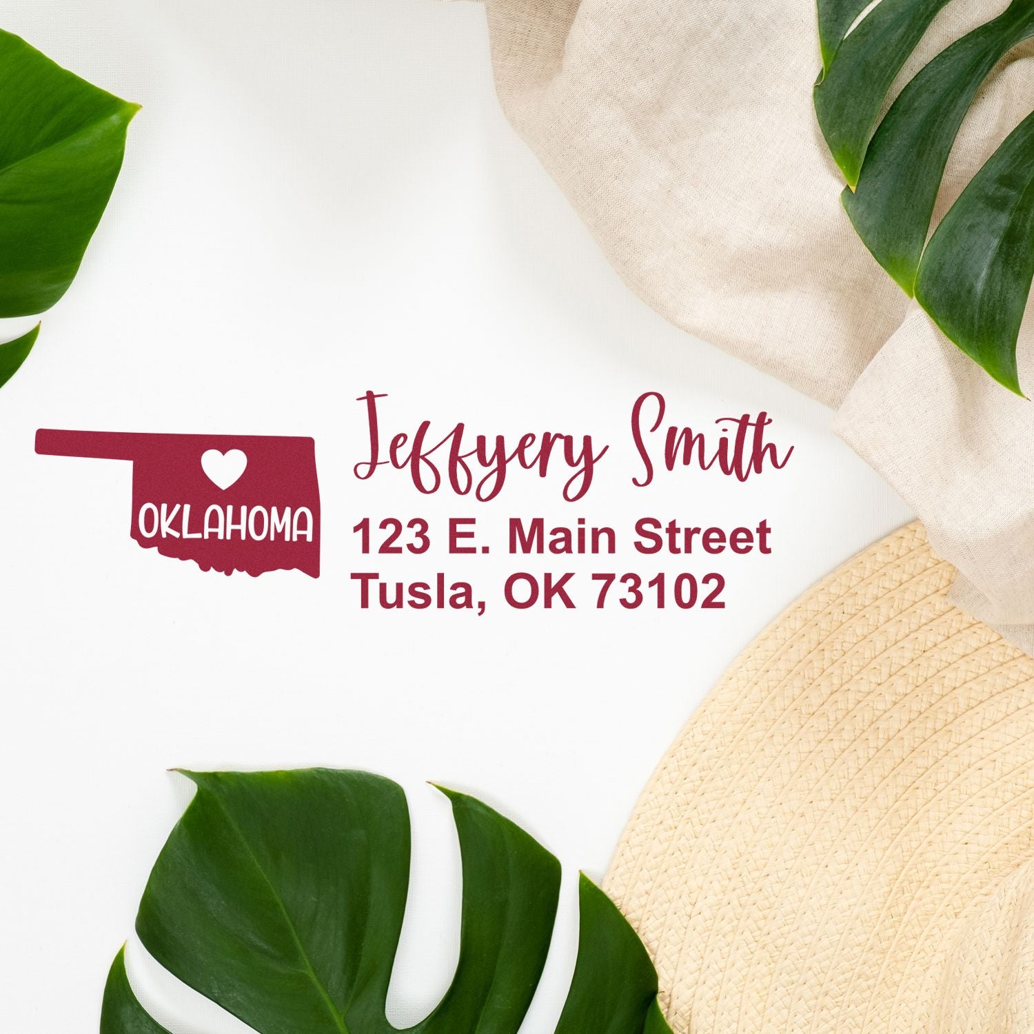 Oklahoma State Love Personalized Address Stamp on a white surface with green leaves and a beige cloth. The stamp features a heart and the word Oklahoma with a sample address in red text.