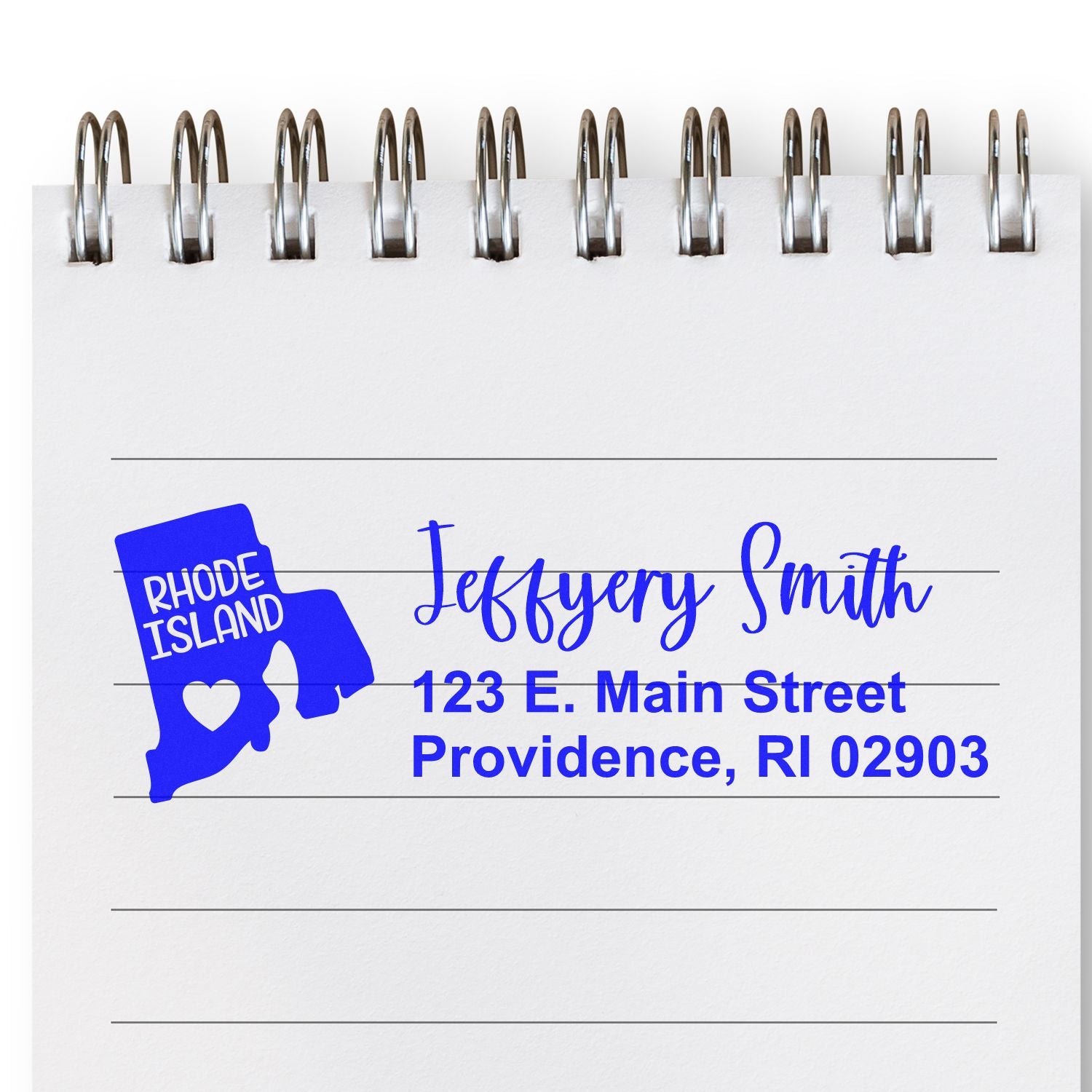 Image of a notepad featuring the Rhode Island State Love Personalized Address Stamp in blue ink, displaying a map outline with a heart and sample address: Jeffery Smith, 123 E. Main Street, Providence, RI 02903.