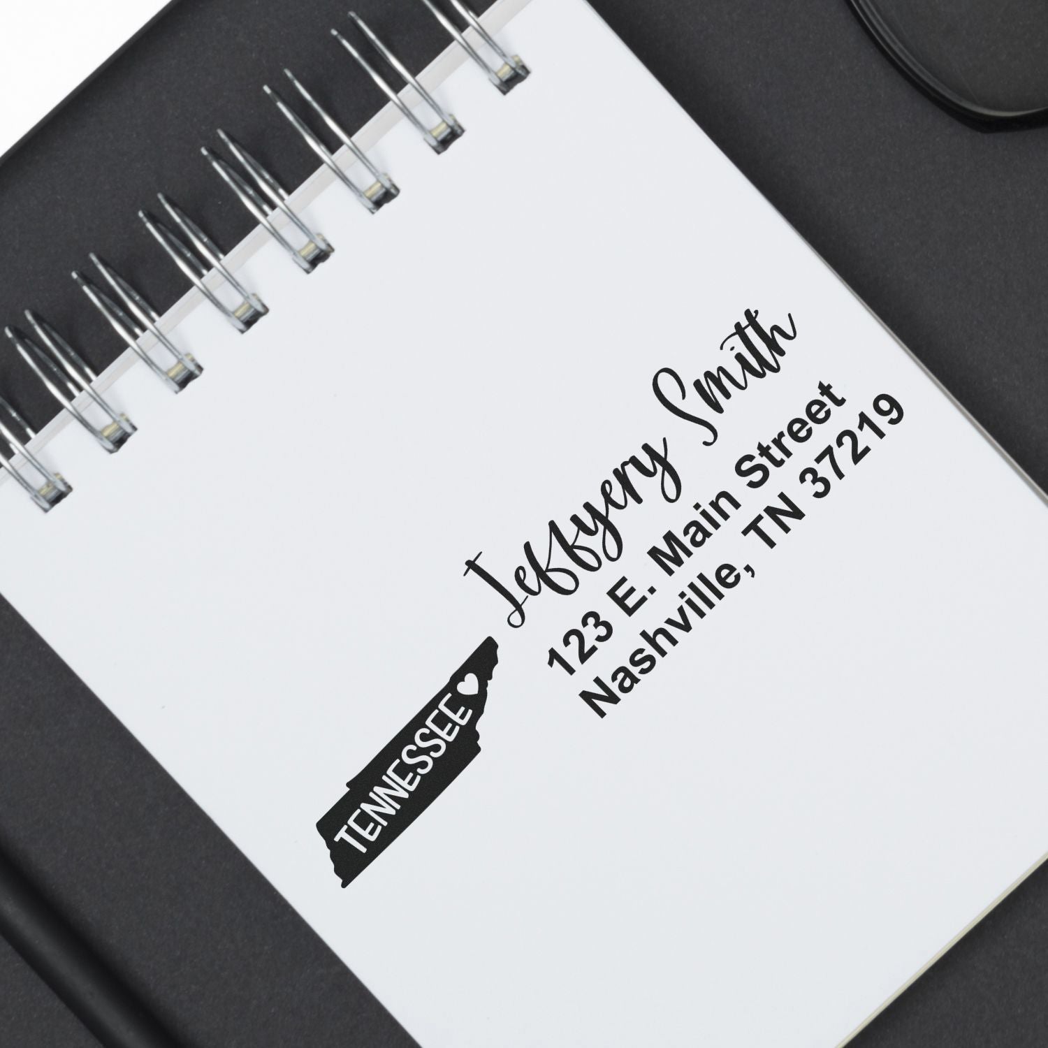 Slim Tennessee Custom Address Stamp for Envelopes displayed on a notebook, showcasing elegant script with a Tennessee state outline. Perfect for personalizing mail with style and precision.