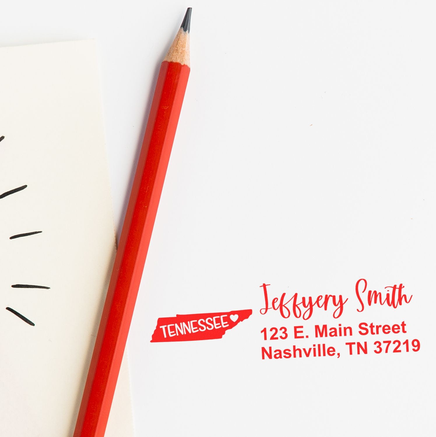 Image of a Slim Tennessee Custom Address Stamp for Envelopes, featuring a red pencil and stamped address: Jeffery Smith, 123 E. Main Street, Nashville, TN 37219 on white paper.