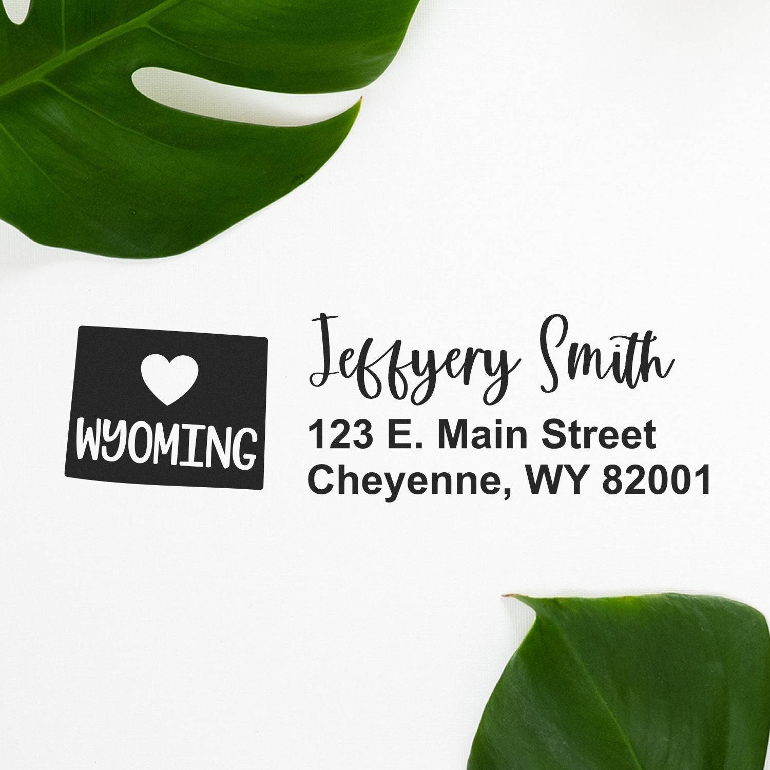 Slim Wyoming Custom Address Stamp for Envelopes displayed on white paper with green leaves, featuring a heart and Wyoming design, personalized with name and address in elegant black font.