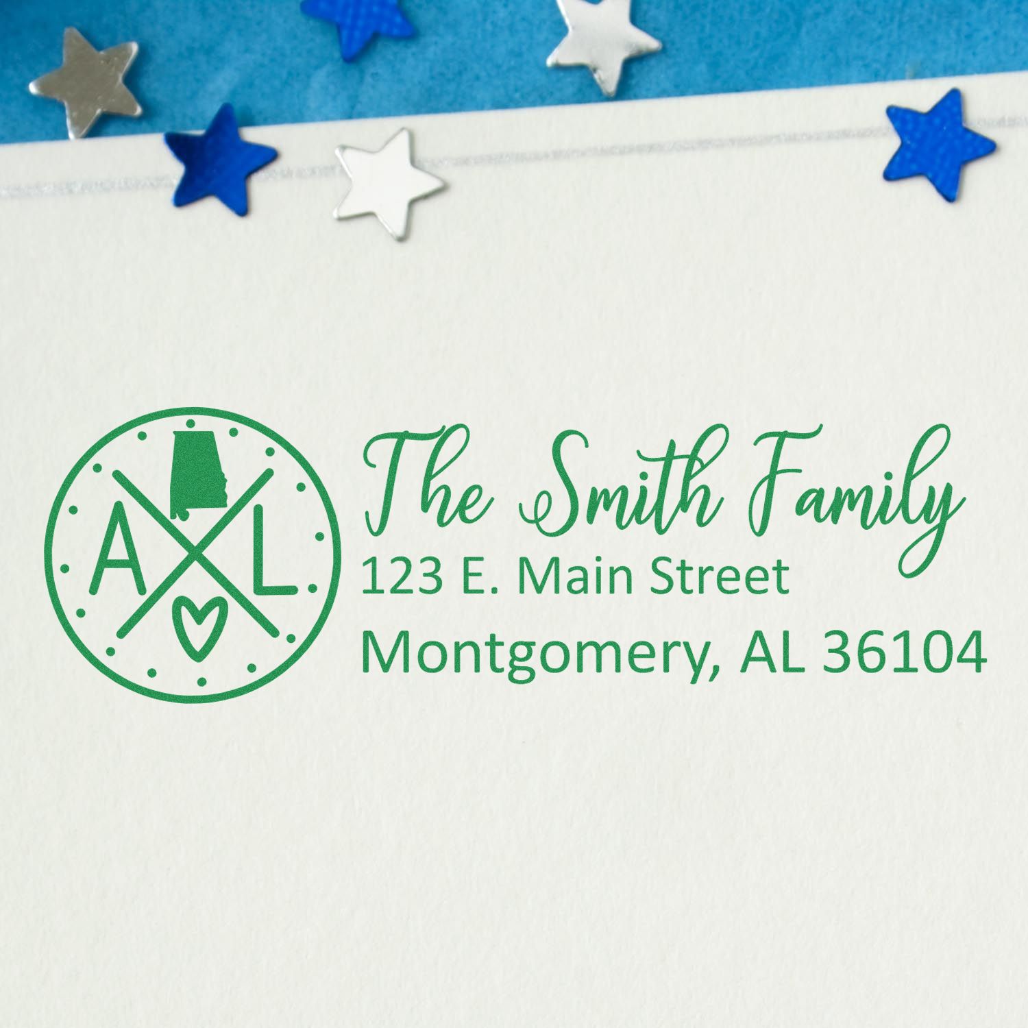 Slim Alabama Customized Pre-Inked Address Stamp on an envelope with a green imprint of The Smith Family and address. Blue and silver star confetti decorates the background.